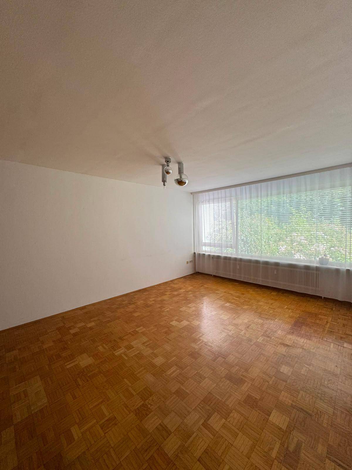 Geräumiges Wohnzimmer mit Fischgrätparkett und großem Fenster, bietet viel Tageslicht.