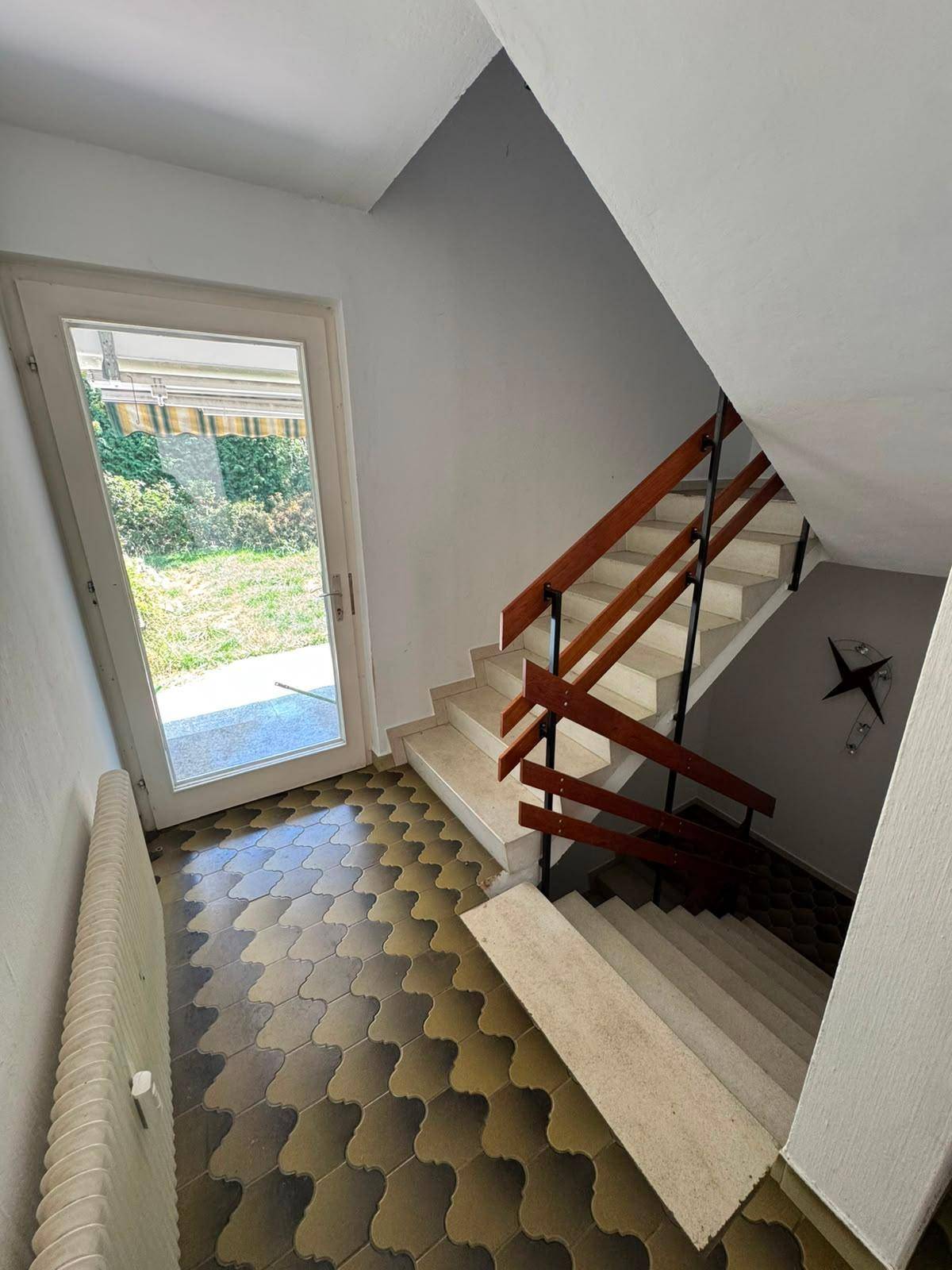 Treppenhaus mit gemustertem Fliesenboden und Holzgeländer, führt zum Gartenausgang.