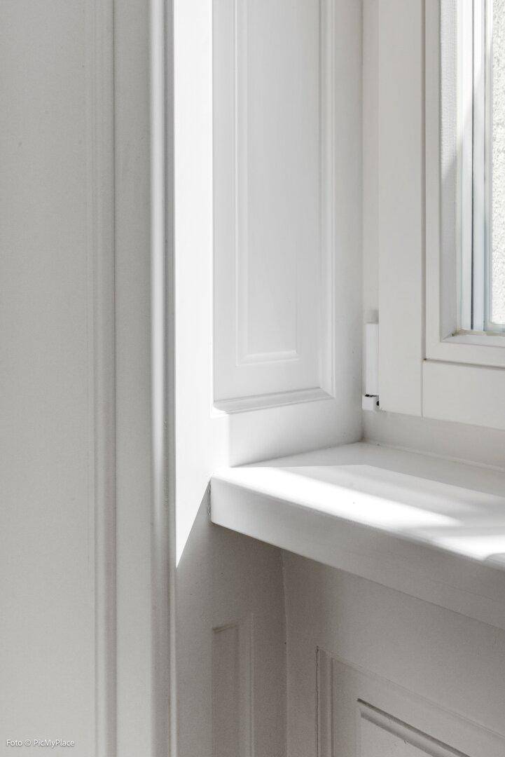 Detailaufnahme eines eleganten weißen Fensterrahmens mit klassischer Holzverkleidung und Fensterbank.