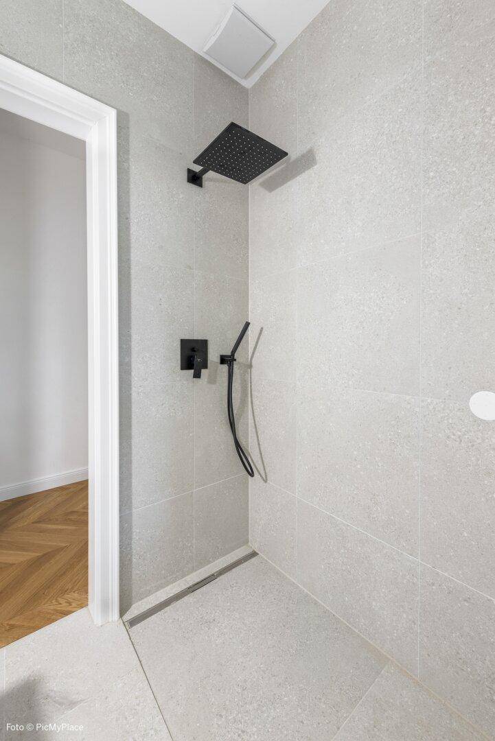 Moderne Duschkabine mit hellgrauen Fliesen und einer stilvollen schwarzen Regendusche.