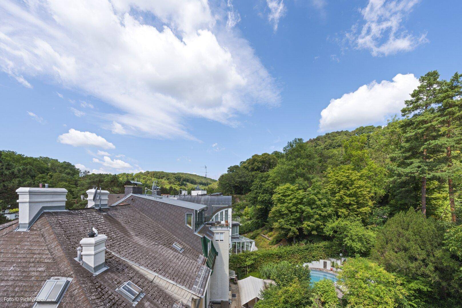 Panoramablick über die Dächer der Häuser und die grüne Hügellandschaft mit einem Pool.