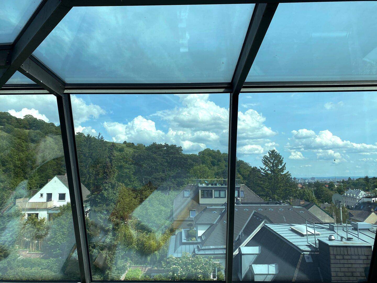 Panoramablick aus großen Glasfenstern auf die grüne Hügellandschaft und die Dächer der Stadt.