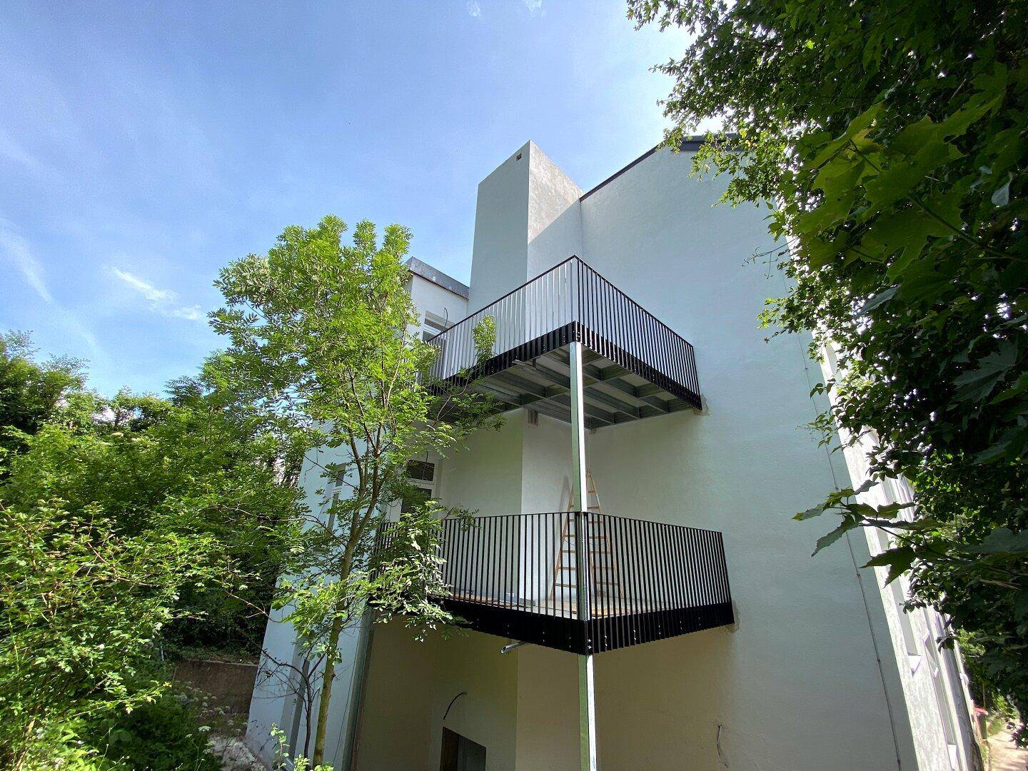 Moderne Gebäudefassade mit mehreren Balkonen und umgebendem Grün.