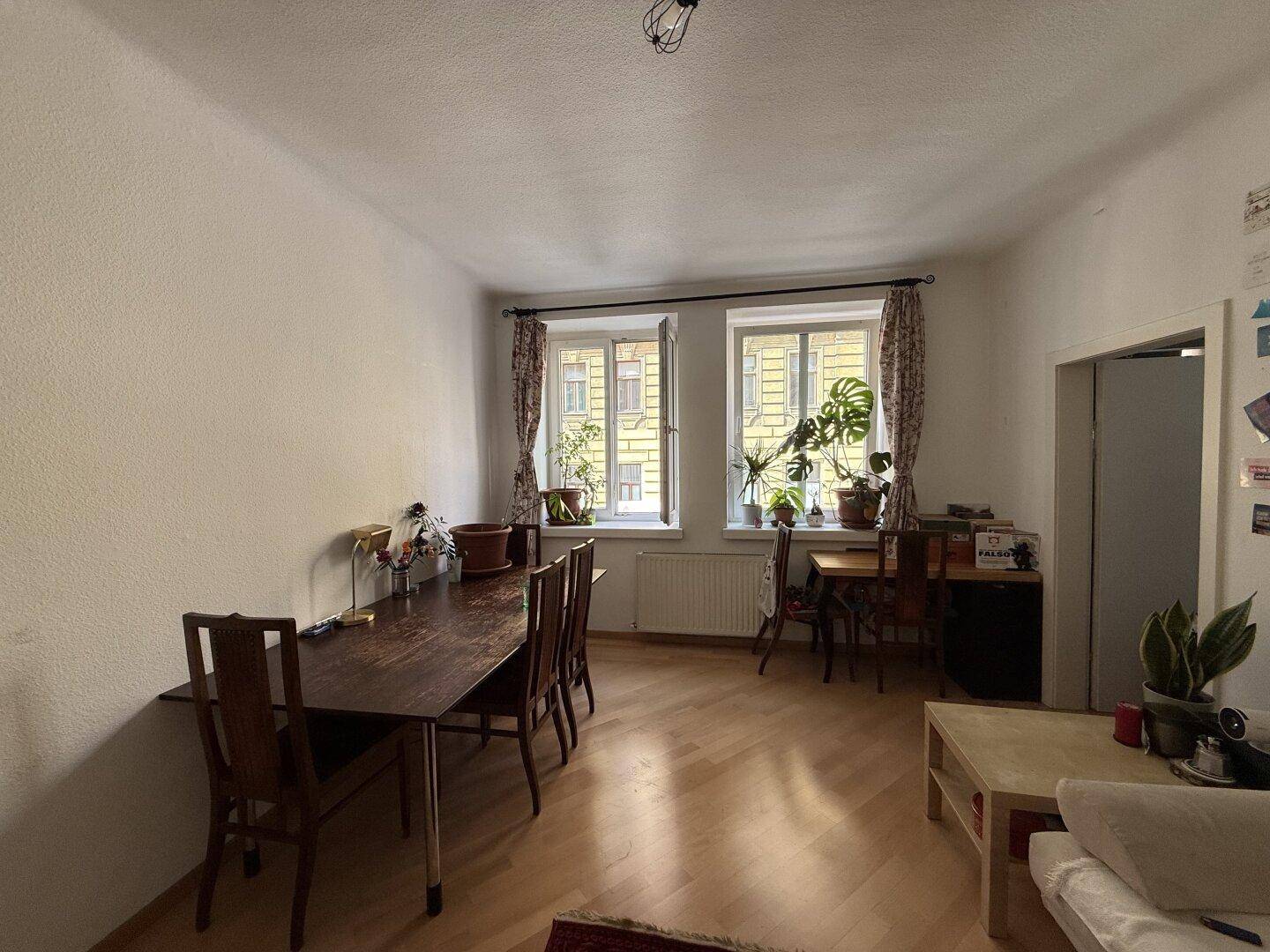 Heller Wohn- und Essbereich mit Parkettboden, großem Esstisch und Blick auf die Straße.