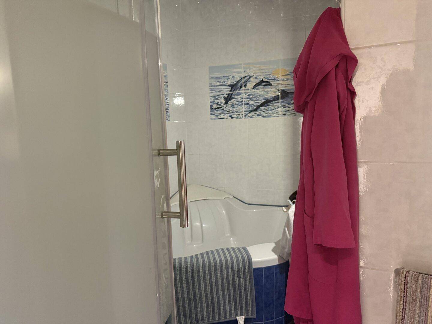 Badezimmer mit Badewanne, Duschabtrennung und verspielten Delfin-Fliesen.