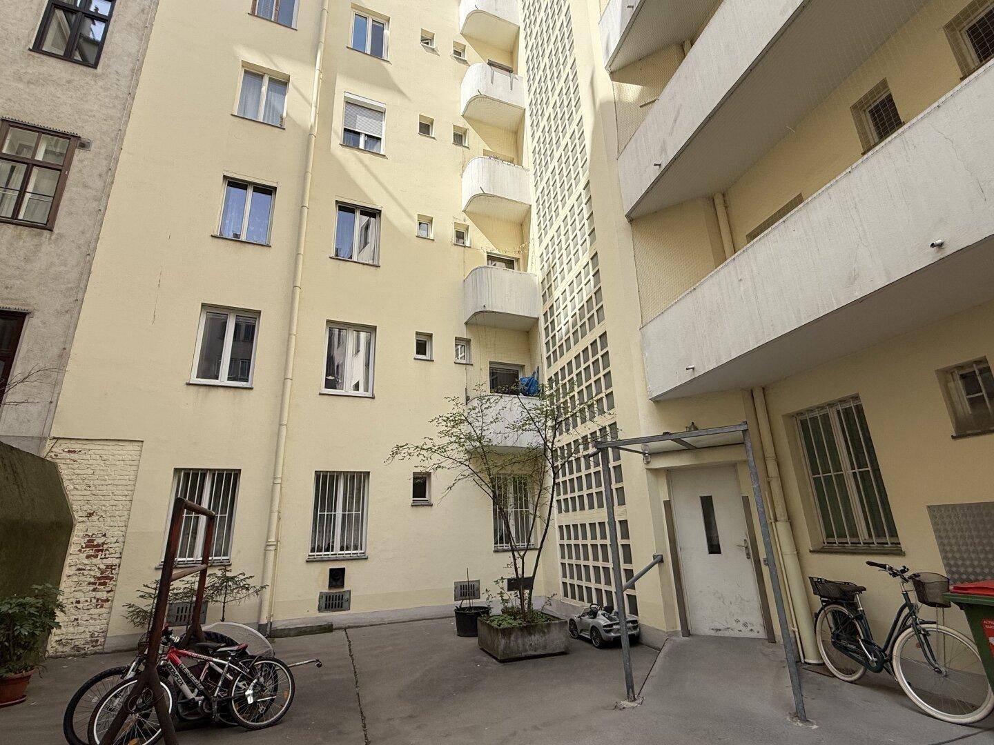 Hinterhof mit Fahrradstellplätzen, Bäumen und Balkonen an der Gebäudefassade.