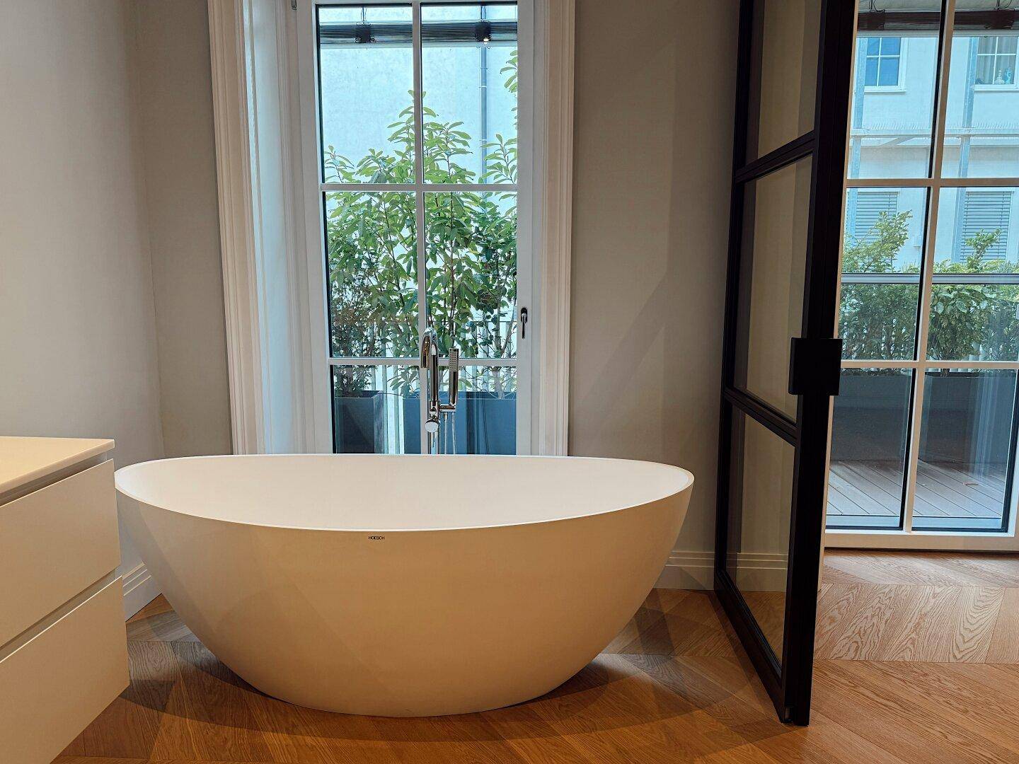 Modernes Badezimmer mit freistehender Badewanne und Zugang zu einem Außenbereich durch große Fenster.