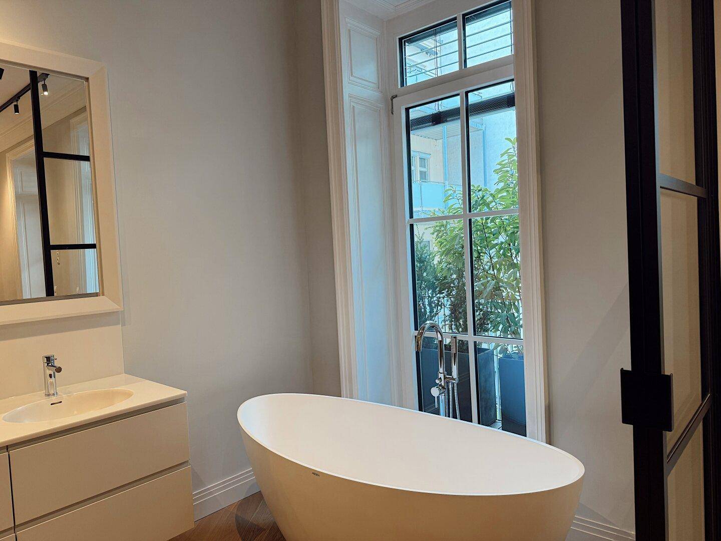 Helles Badezimmer mit freistehender Badewanne, Waschtisch und großem Fenster.