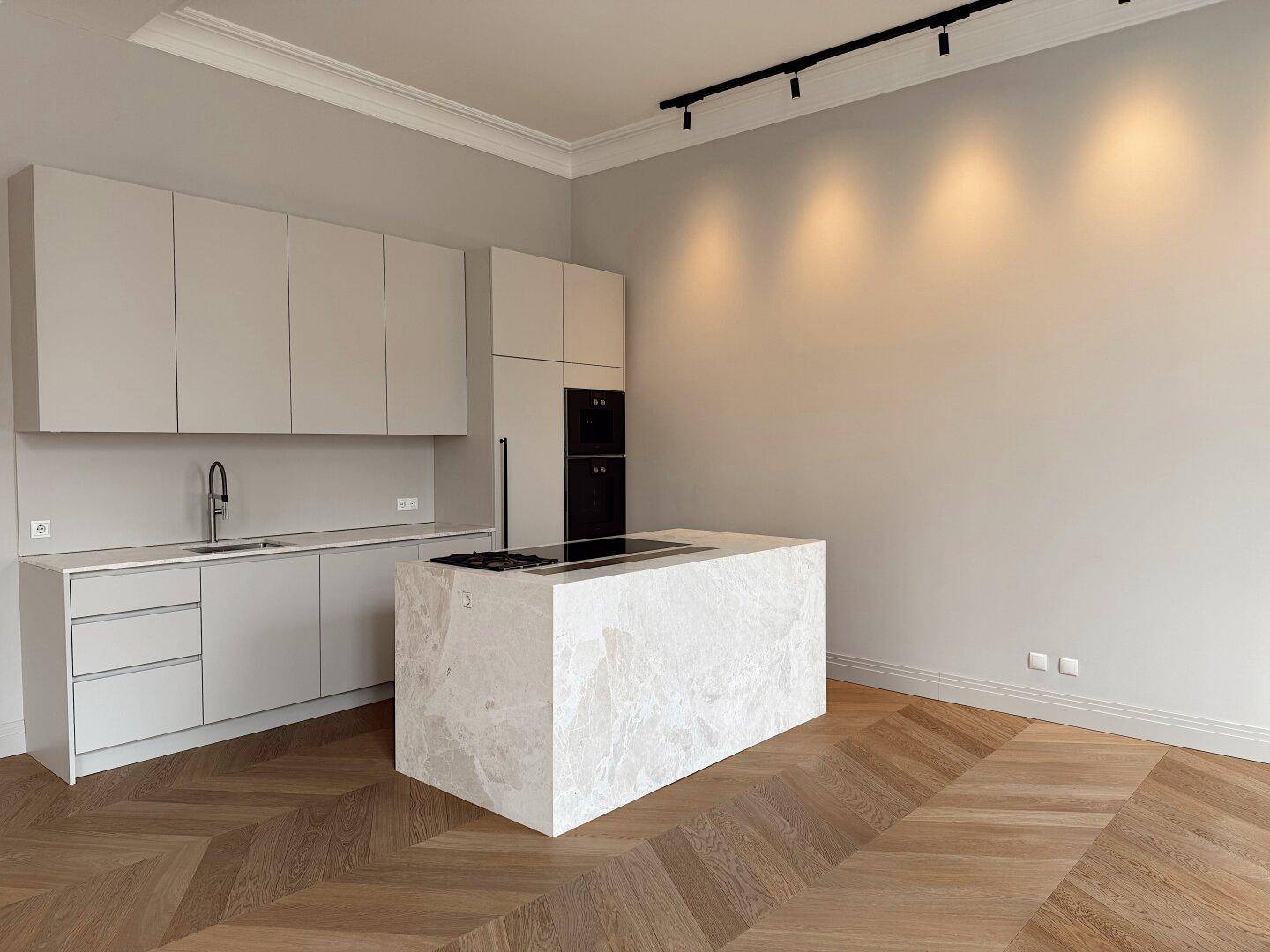 Geräumige, moderne Küche mit Kochinsel, Einbaugeräten und elegantem Fischgrätparkett.
