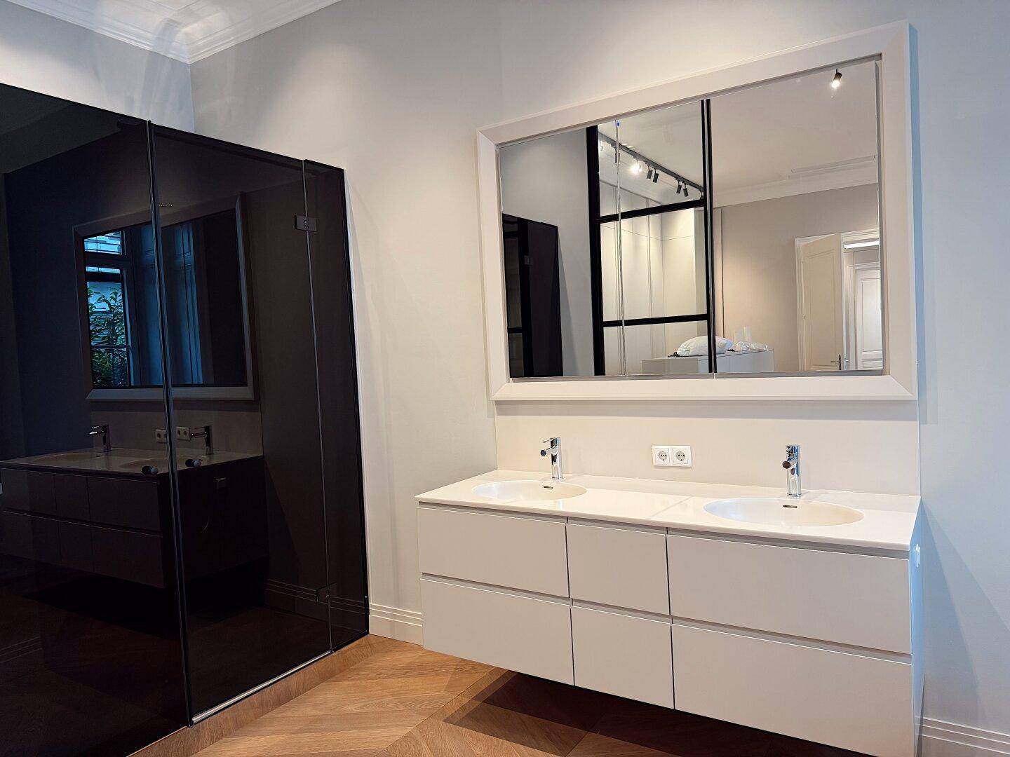 Elegantes Badezimmer mit Doppelwaschbecken, großem Spiegel und dunklen, reflektierenden Oberflächen.