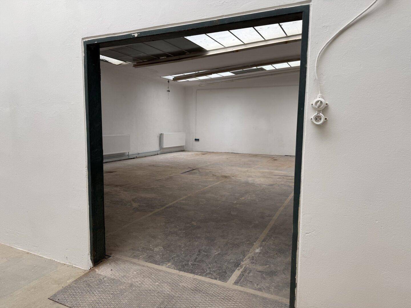 Blick durch eine breite Tür mit Rampe in einen hellen, leeren Gewerberaum mit Oberlichtern und Betonboden.