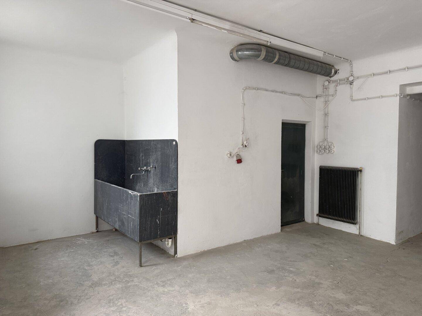 Funktionsraum mit großem Waschbecken, sichtbaren Rohrleitungen und einem schwarzen Heizkörper, ideal für gewerbliche Nutzung.