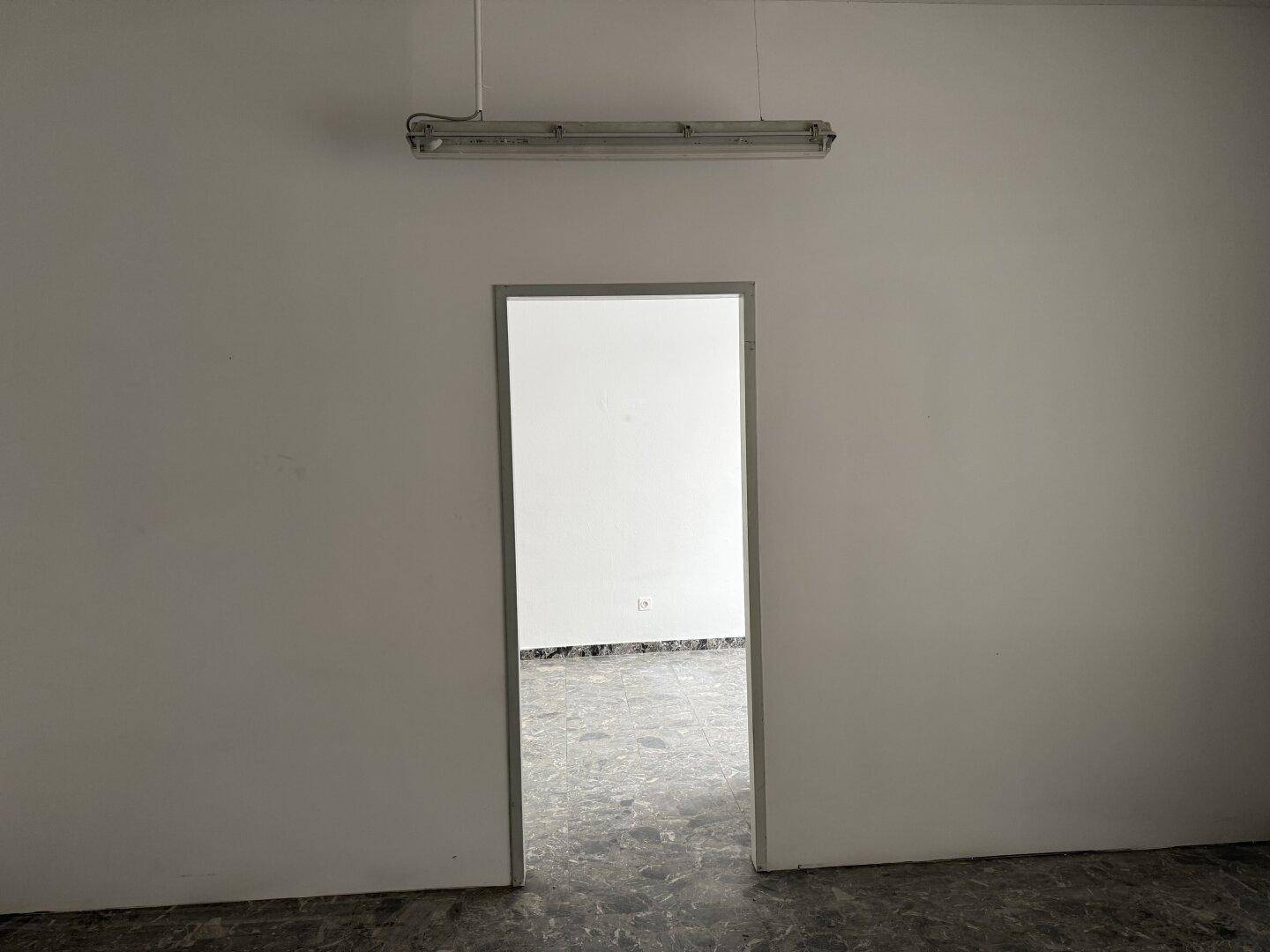 Blick durch eine Tür in einen weiteren Raum mit dunklem, gesprenkeltem Fliesenboden und einer Deckenleuchte.