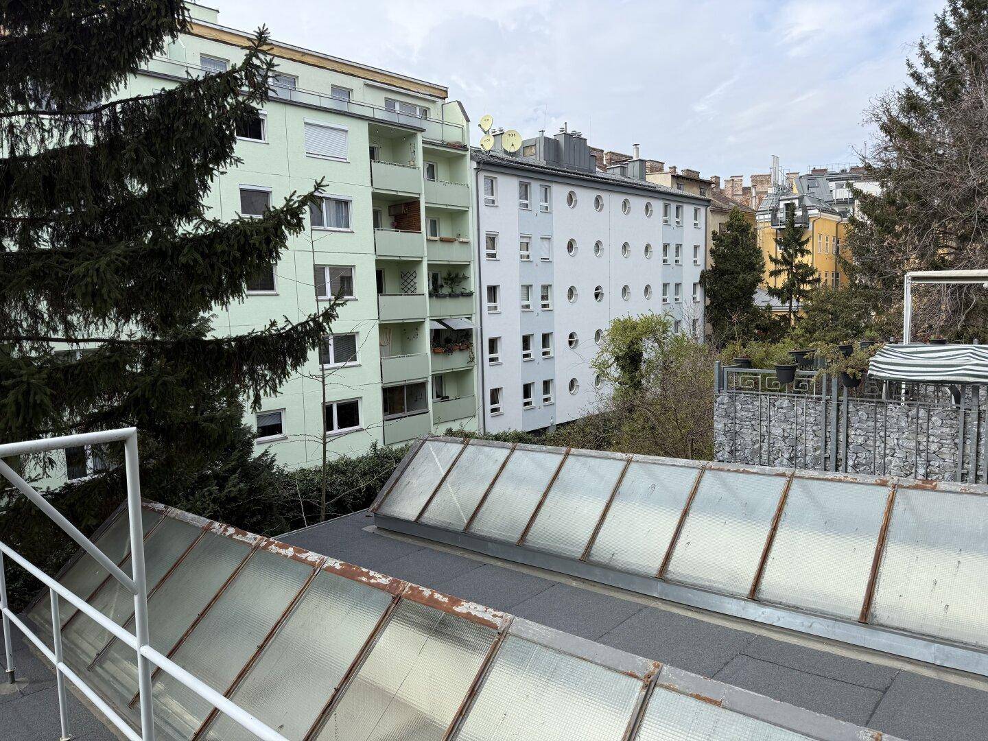 Blick von oben auf Dächer mit Oberlichtern, Bäume und Wohngebäude in einer städtischen Umgebung.