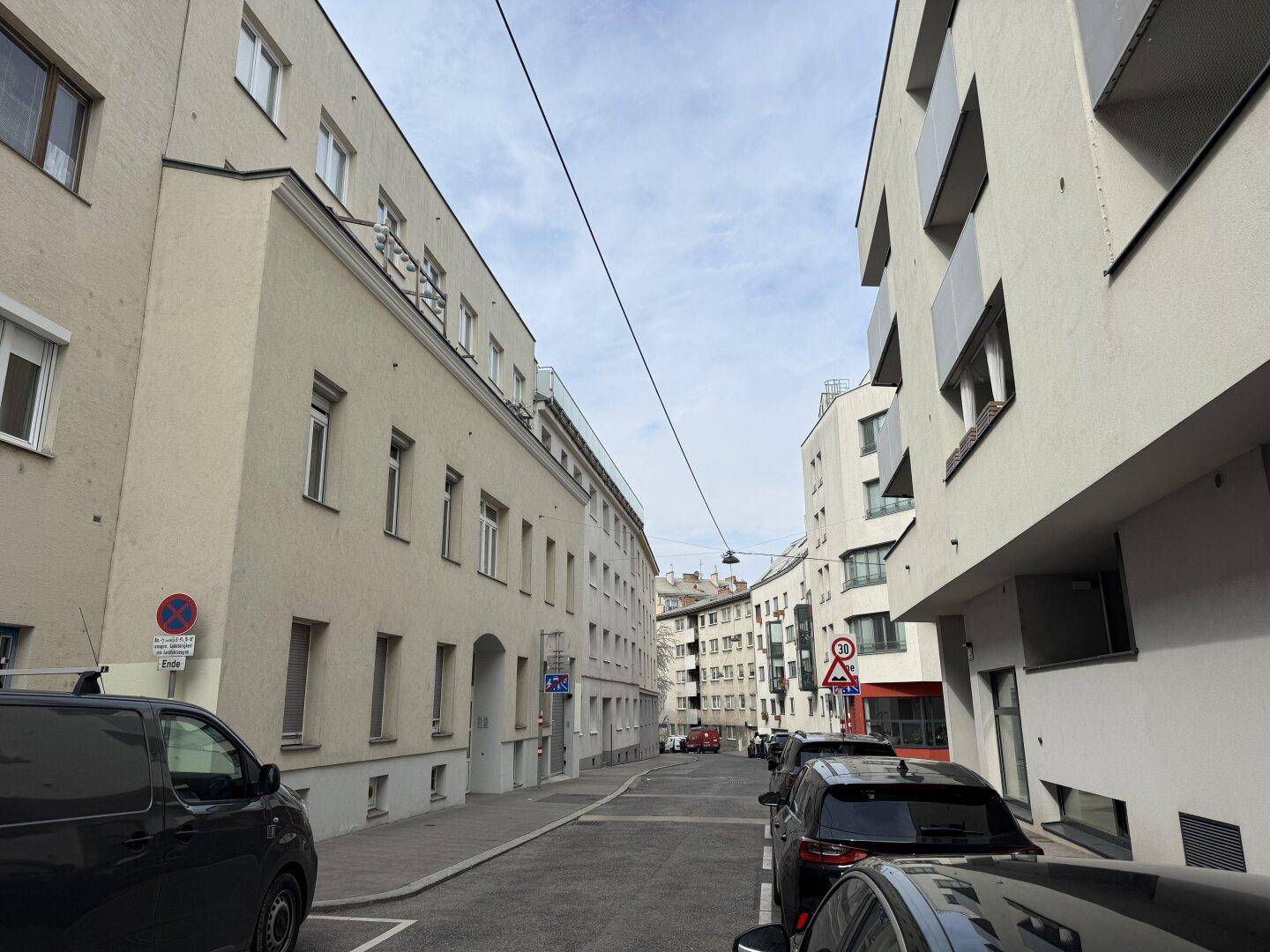 Eine ruhige Wohnstraße mit geparkten Autos und mehrstöckigen Gebäuden unter einem bewölkten Himmel.