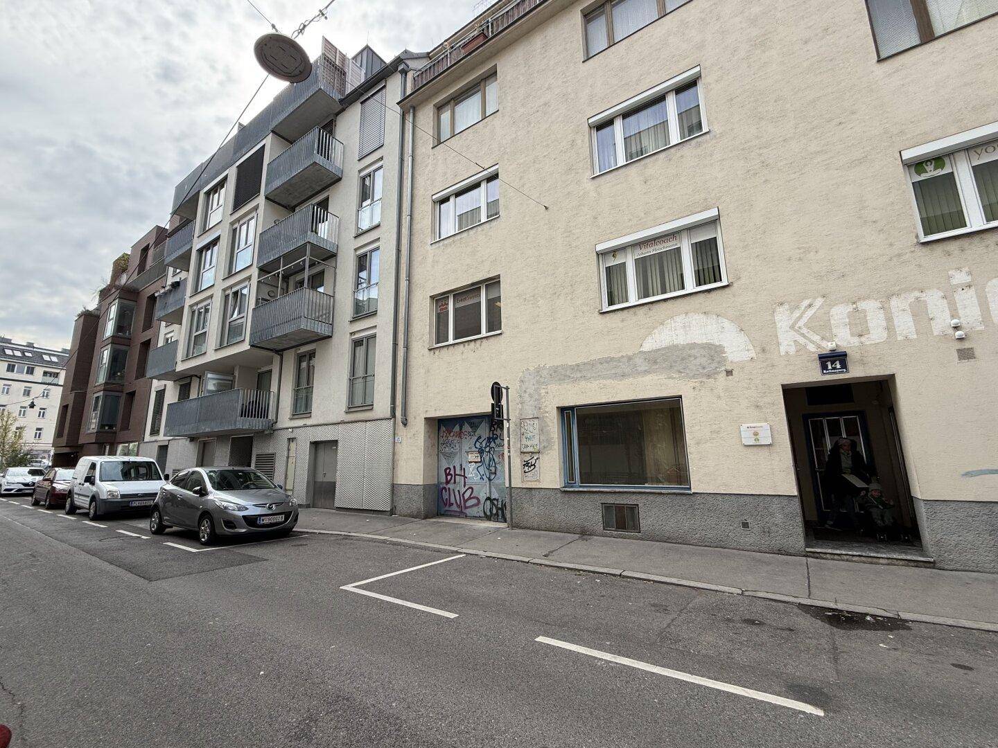 Gebäudefassade auf Straßenniveau mit einem ehemaligen Geschäft, Graffiti und geparkten Autos auf der Straße.