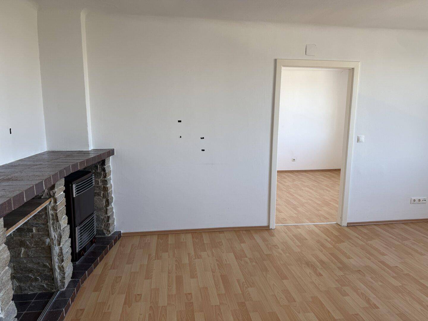 Leerer Raum mit Laminatboden und einer dekorativen Steinverkleidung, möglicherweise ein Kamin.