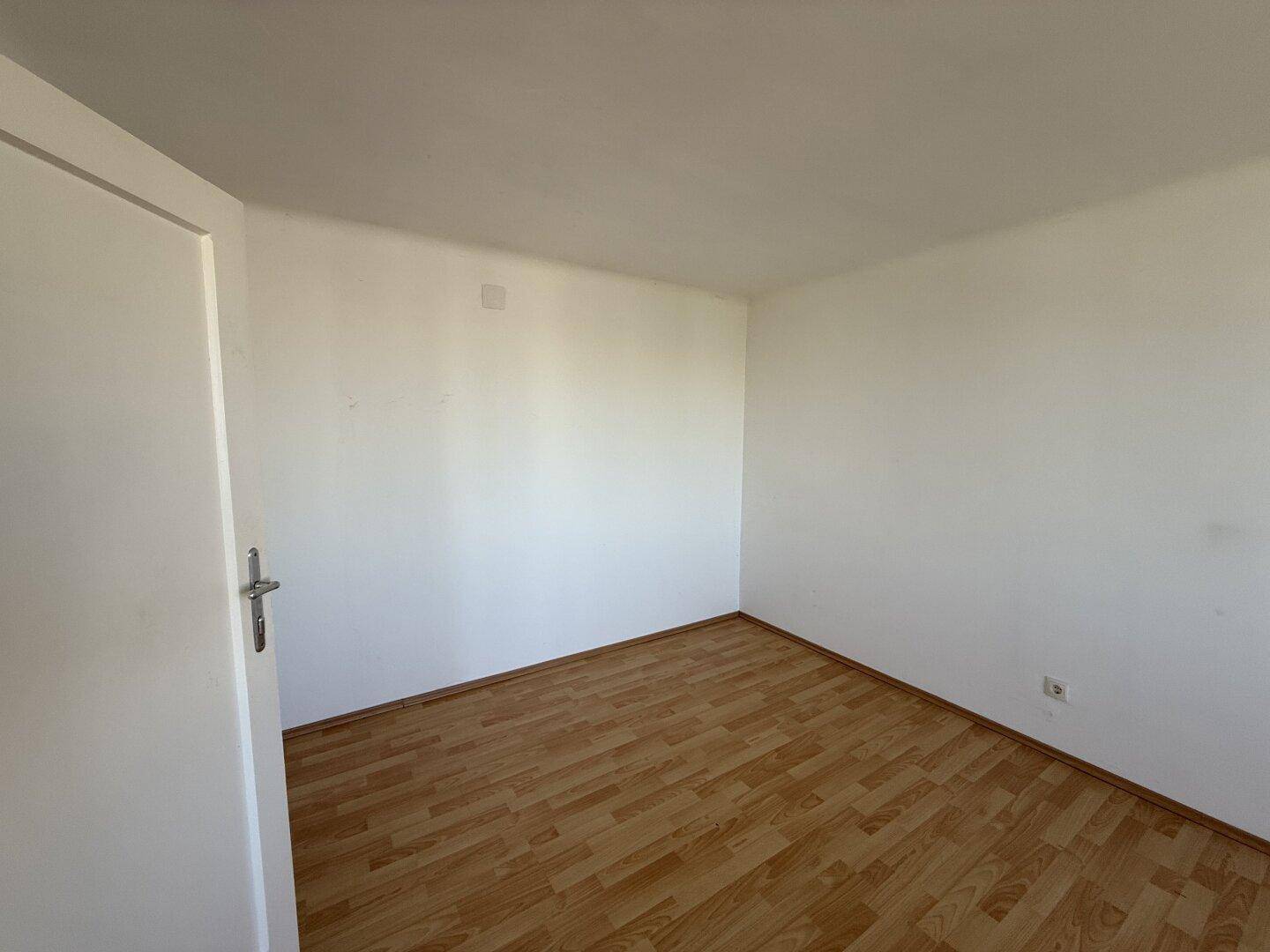 Kleiner, heller Raum mit Laminatboden und weißen Wänden, ideal als Schlaf- oder Arbeitszimmer.