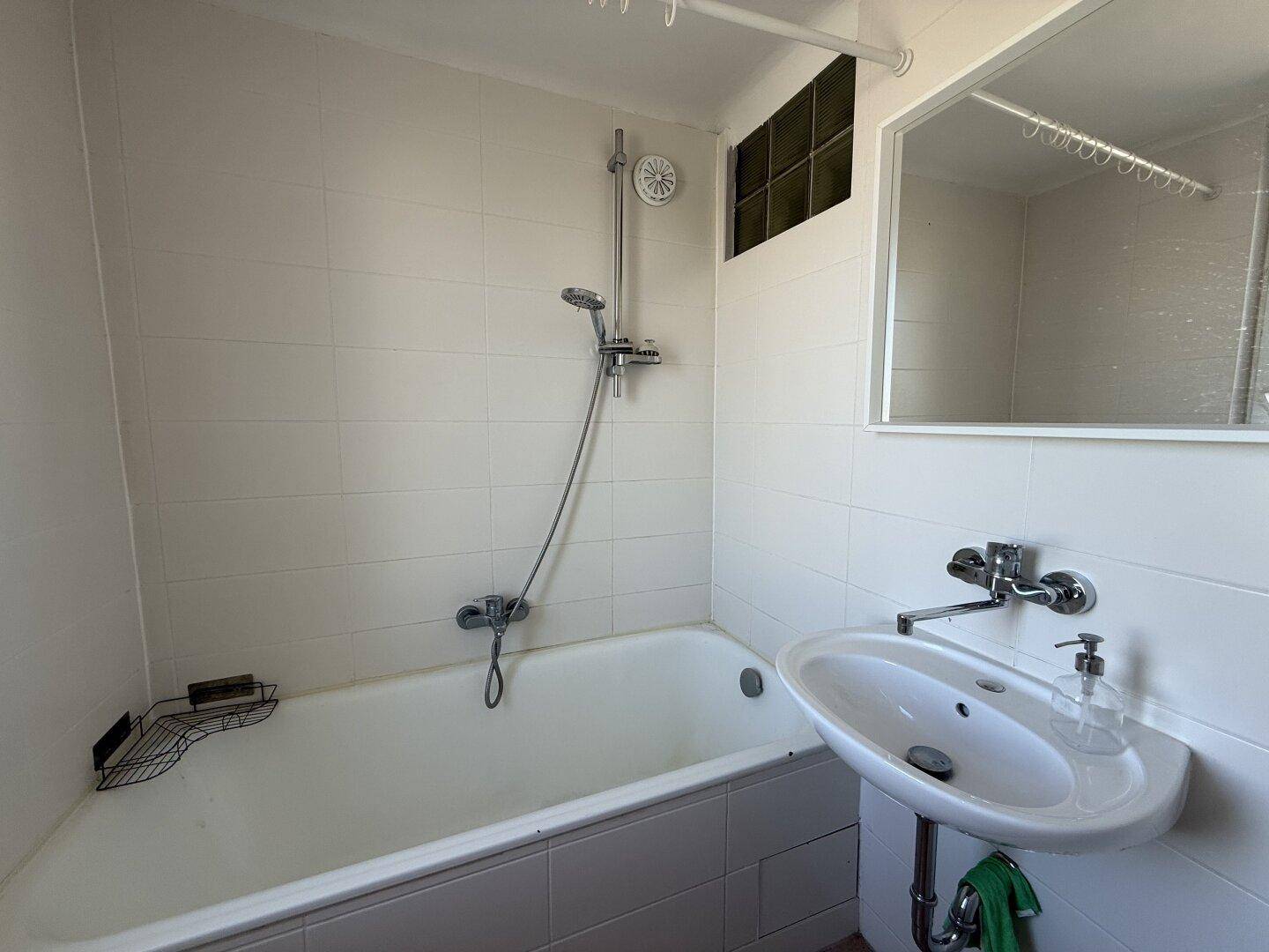 Badezimmer mit weiß gefliesten Wänden, Badewanne mit Duschfunktion und Waschbecken.