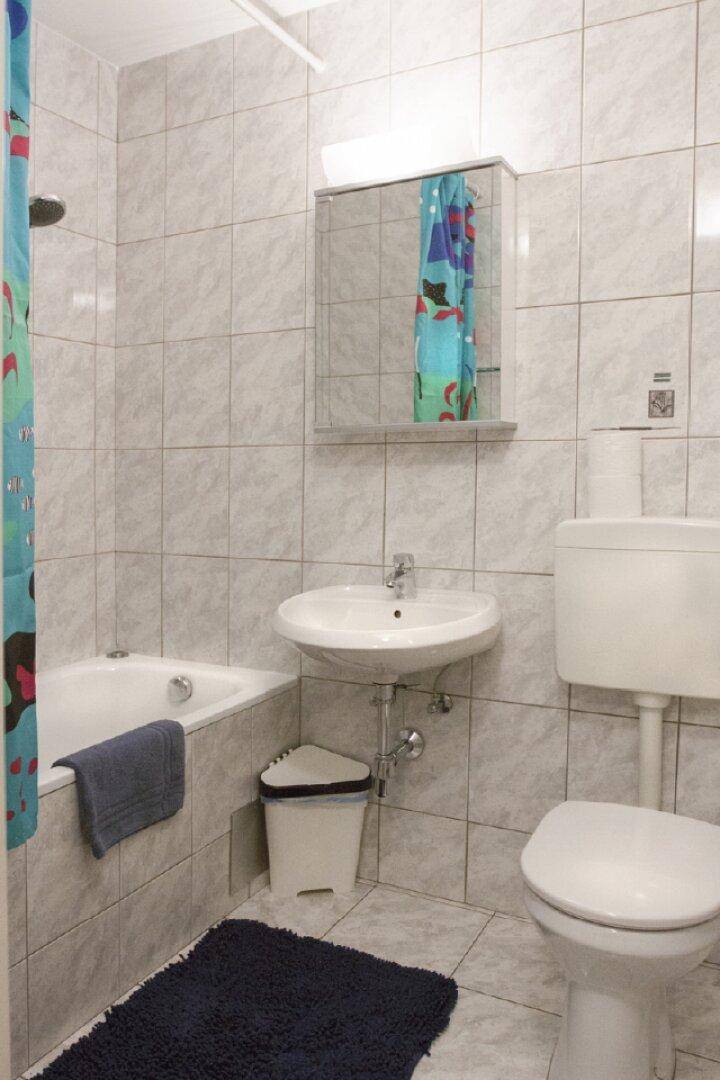 Gefliestes Badezimmer mit Badewanne, Waschbecken, Toilette und Spiegelschrank.