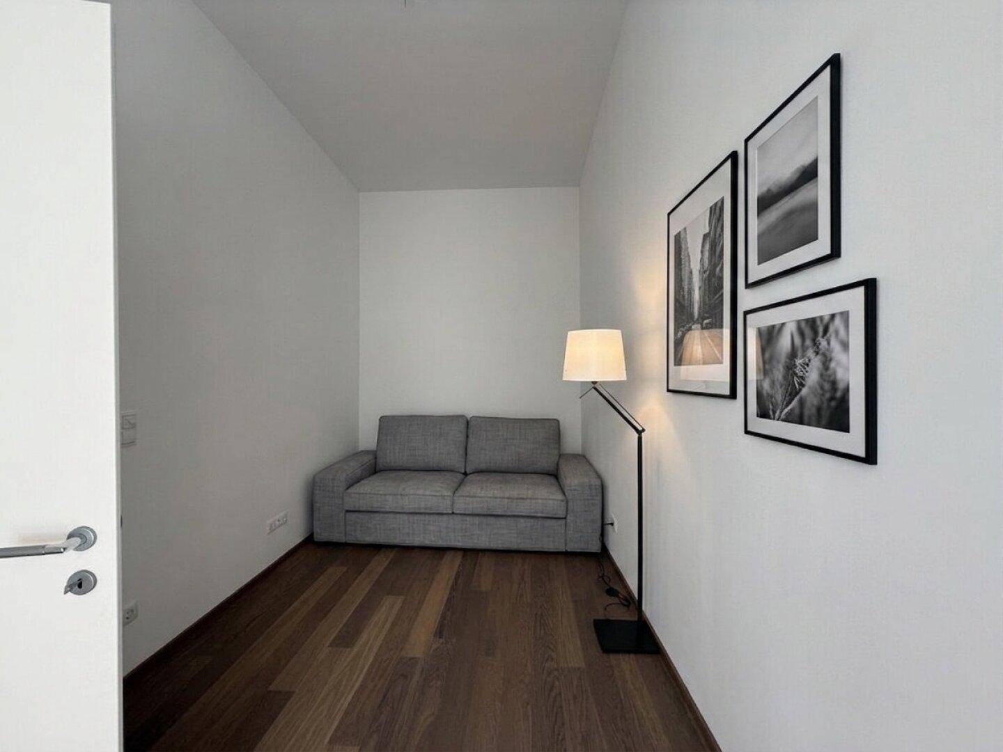 Gemütlicher Wohnbereich mit grauem Sofa, Stehlampe und dunklem Holzboden.