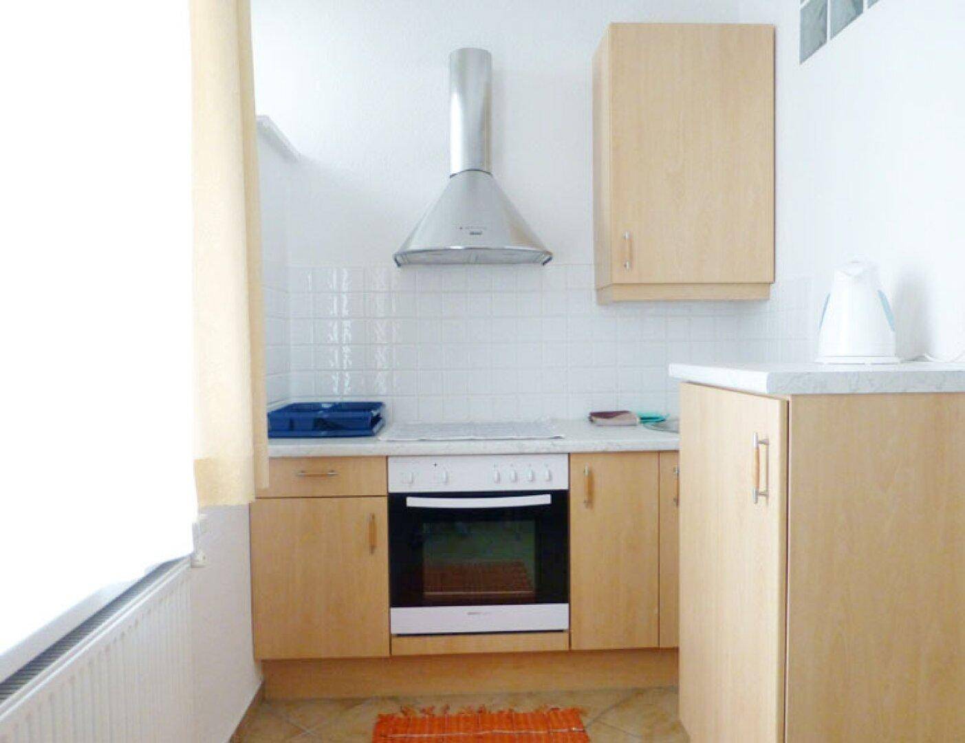 Funktionale Küchenzeile mit hellen Holzschränken, Herd, Backofen und Dunstabzugshaube.
