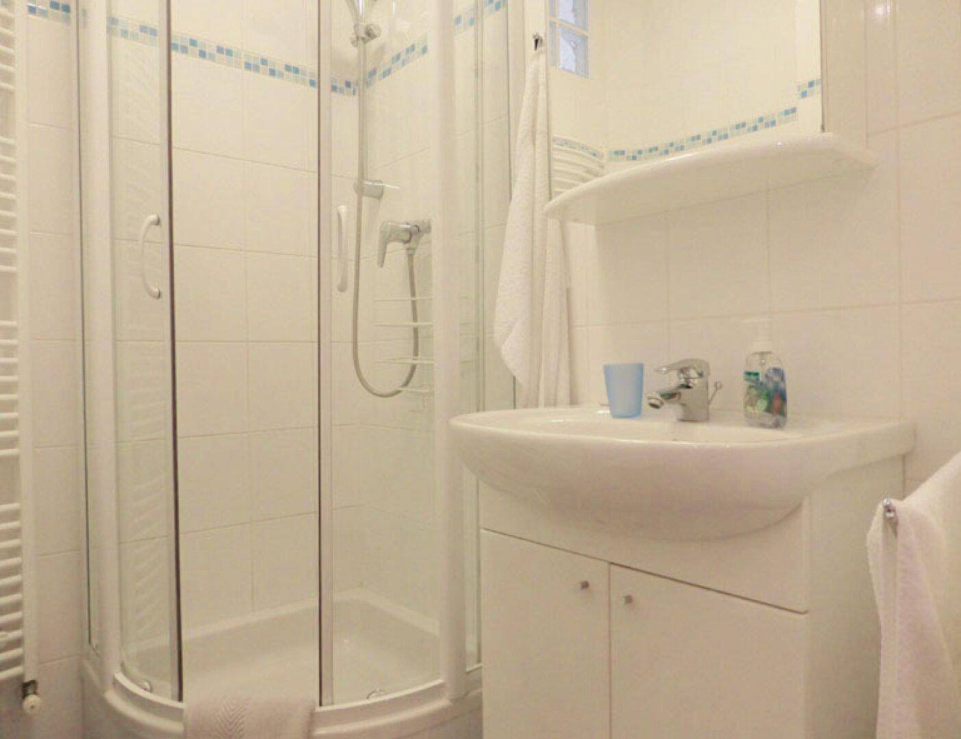Helles Badezimmer mit Duschkabine, Waschbecken und einem beheizten Handtuchhalter.