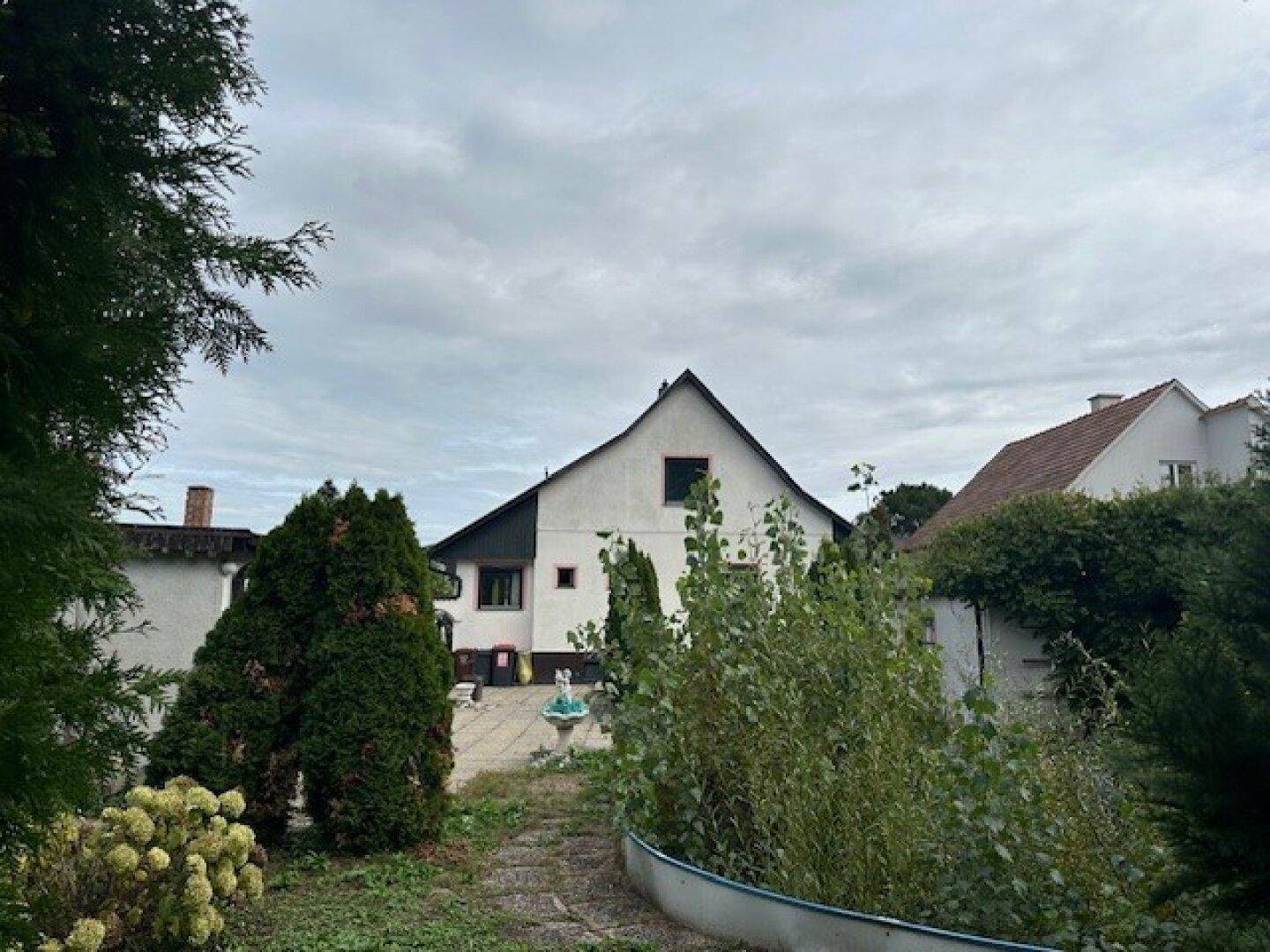 Blick auf die Rückseite des Hauses vom Garten aus, mit einem kleinen Brunnen und Pflanzen.
