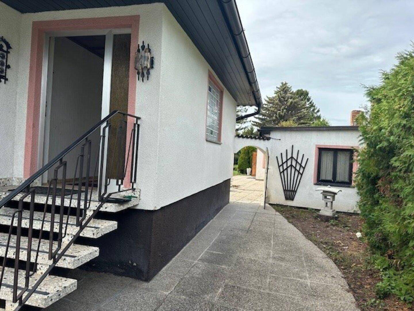 Eingangsbereich des Hauses mit Steintreppe und gepflastertem Weg zu einem Nebengebäude.