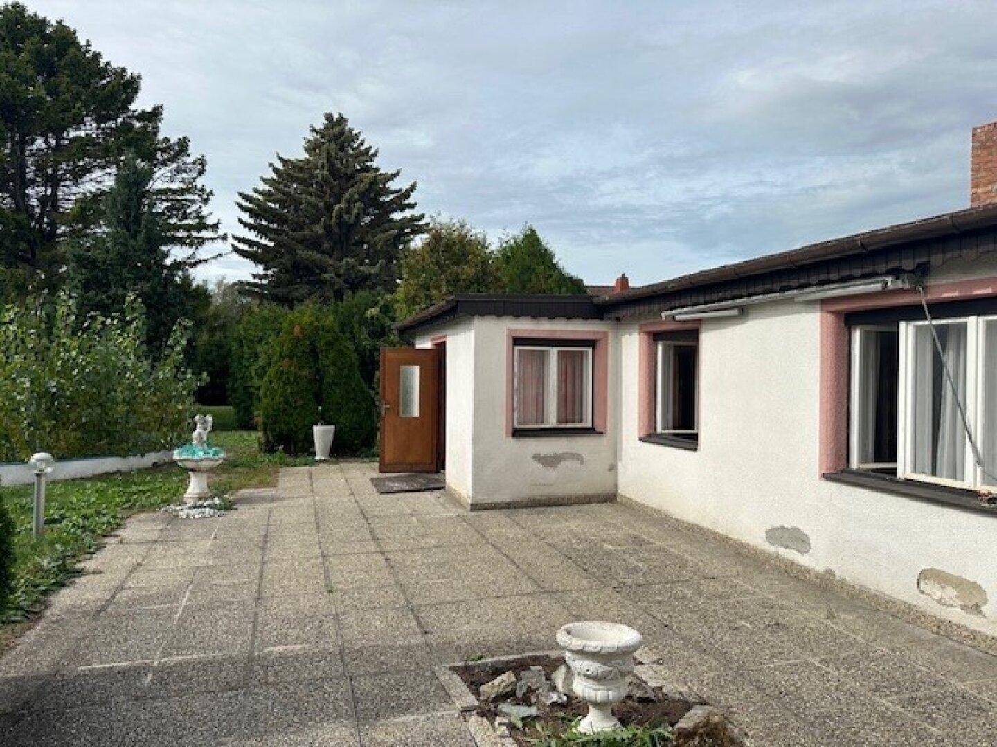 Gepflasterte Terrasse am Haus mit einem kleinen Anbau und dekorativen Elementen.