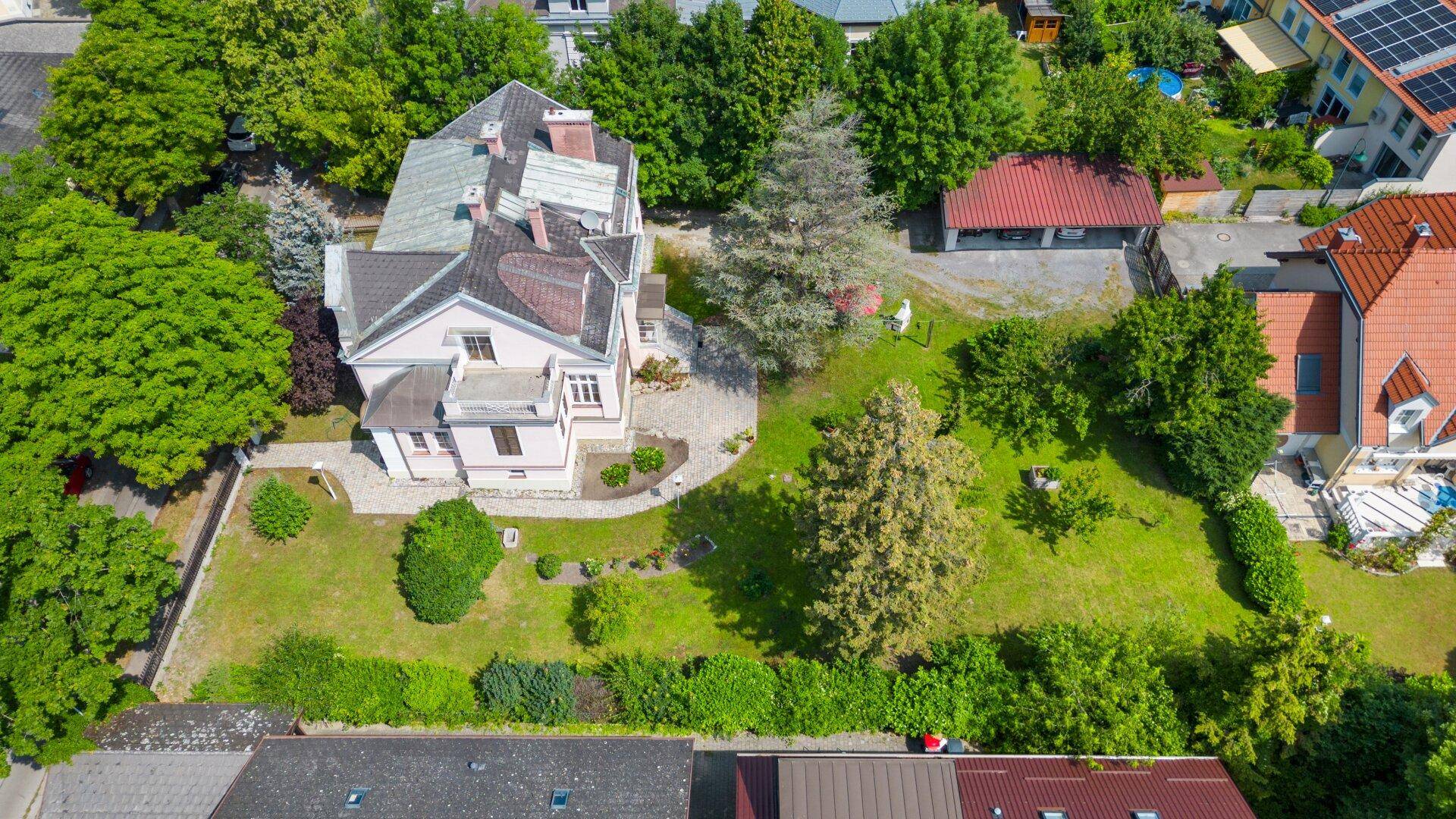 Luftaufnahme des Anwesens mit großem Garten, altem Baumbestand und umliegender Bebauung.