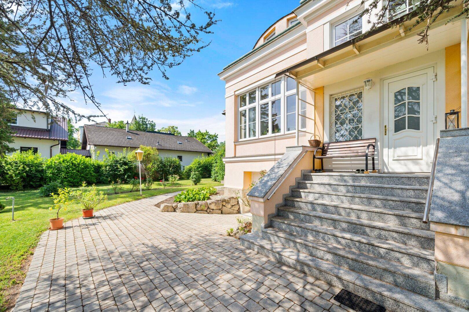 Eingangsbereich mit Steintreppe und gepflastertem Weg, umgeben von einem gepflegten Garten.