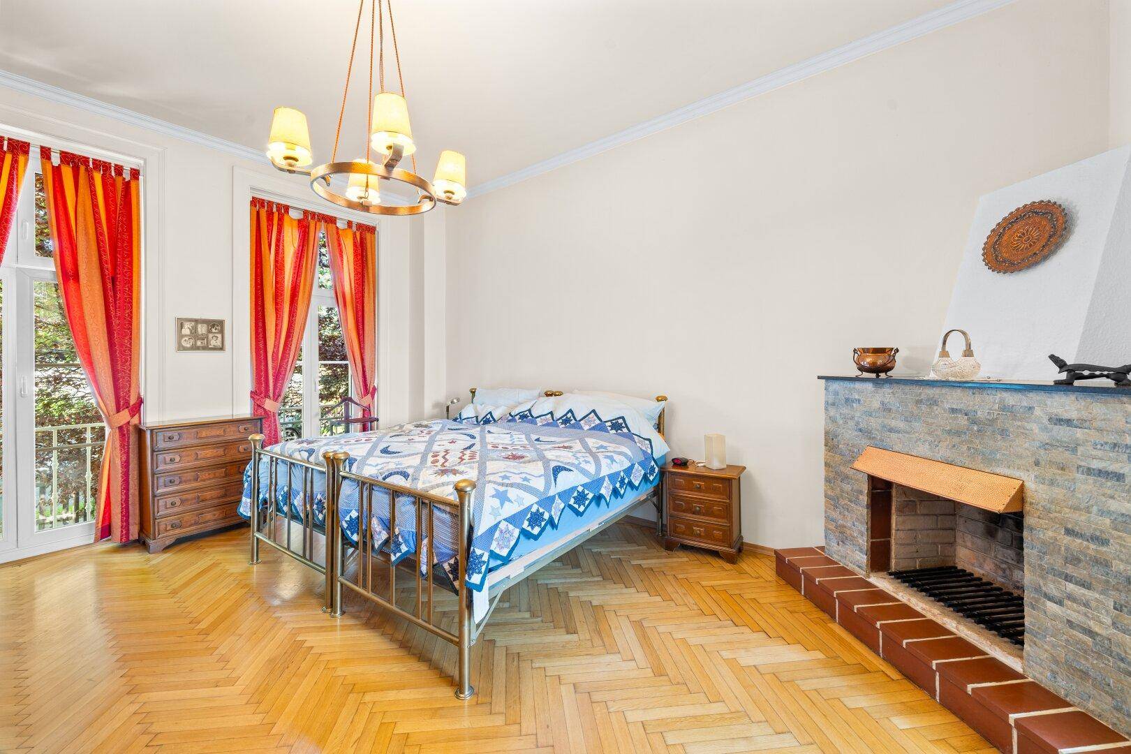 Gemütliches Schlafzimmer mit Fischgrätparkett, Kamin und Zugang zu einem französischen Balkon.