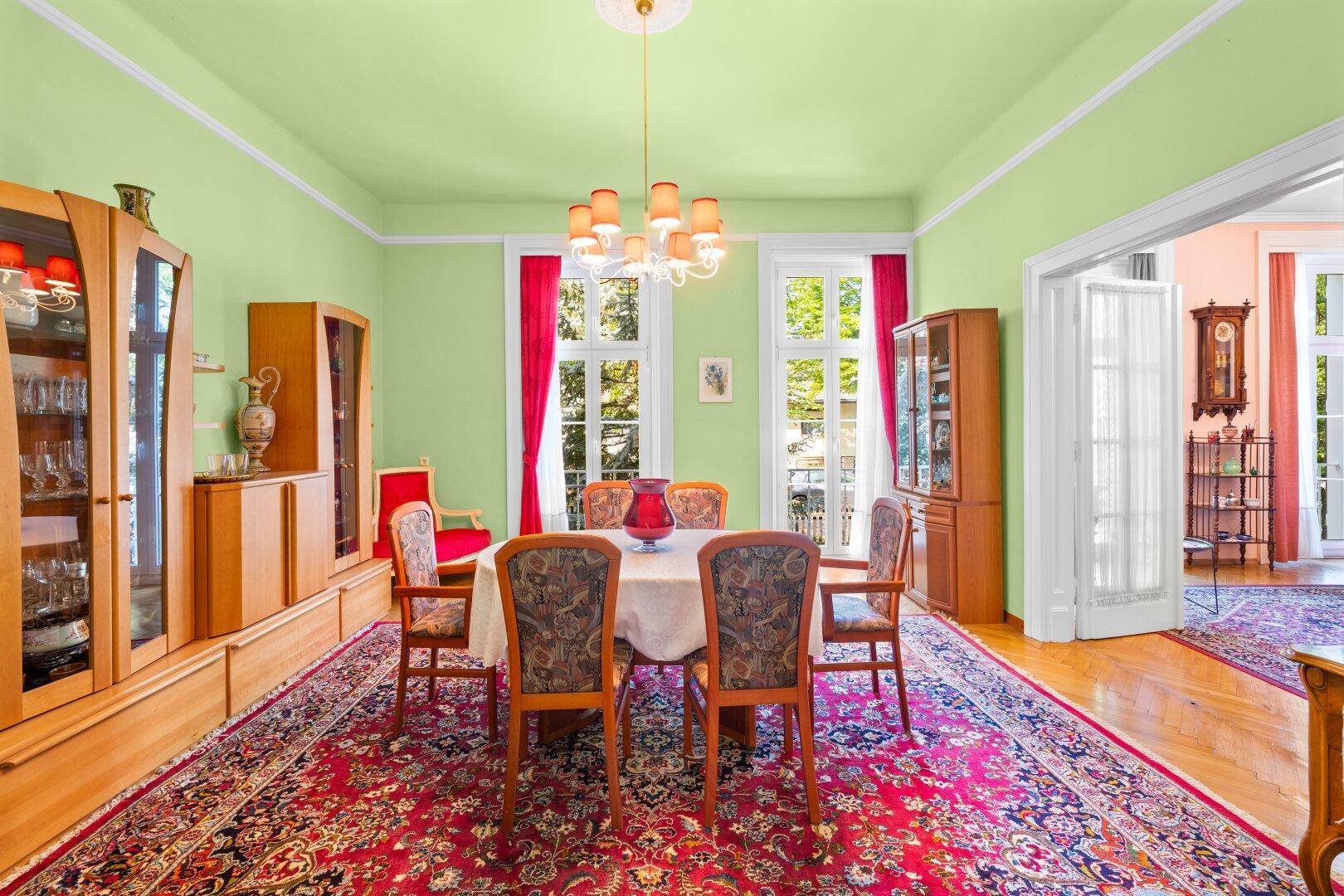 Elegantes Esszimmer mit grün gestrichenen Wänden, Teppich und Zugang zum Wohnzimmer.