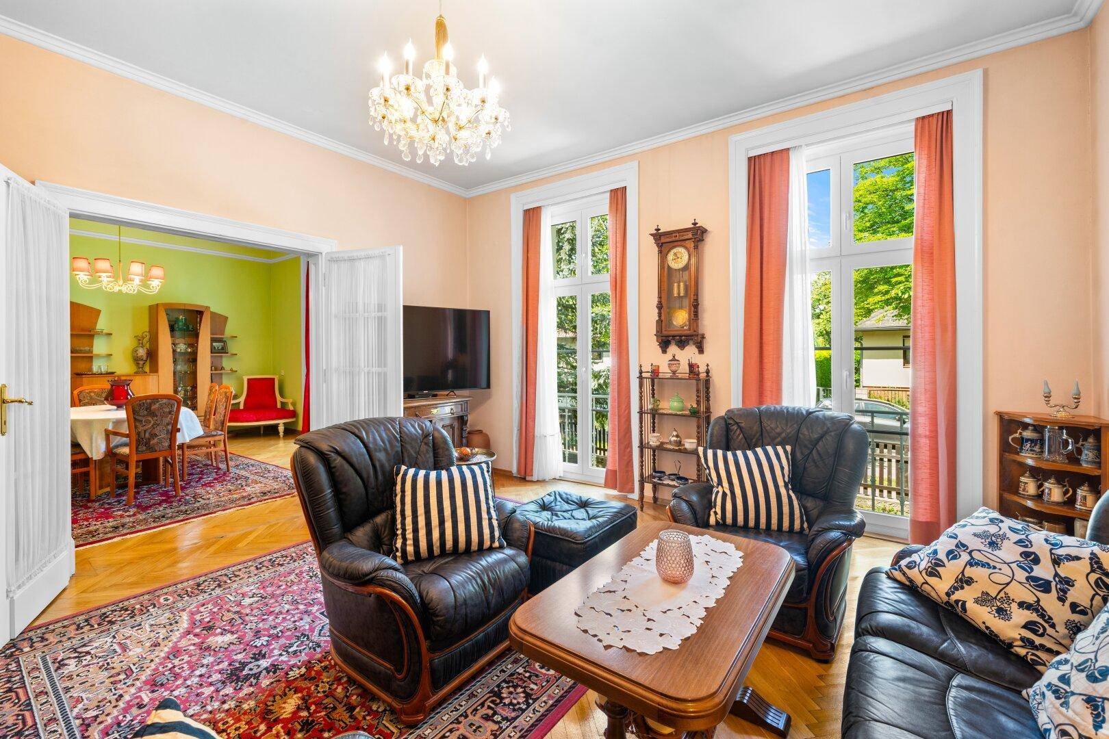 Klassisches Wohnzimmer mit Ledersesseln, Kronleuchter und Zugang zum Esszimmer.