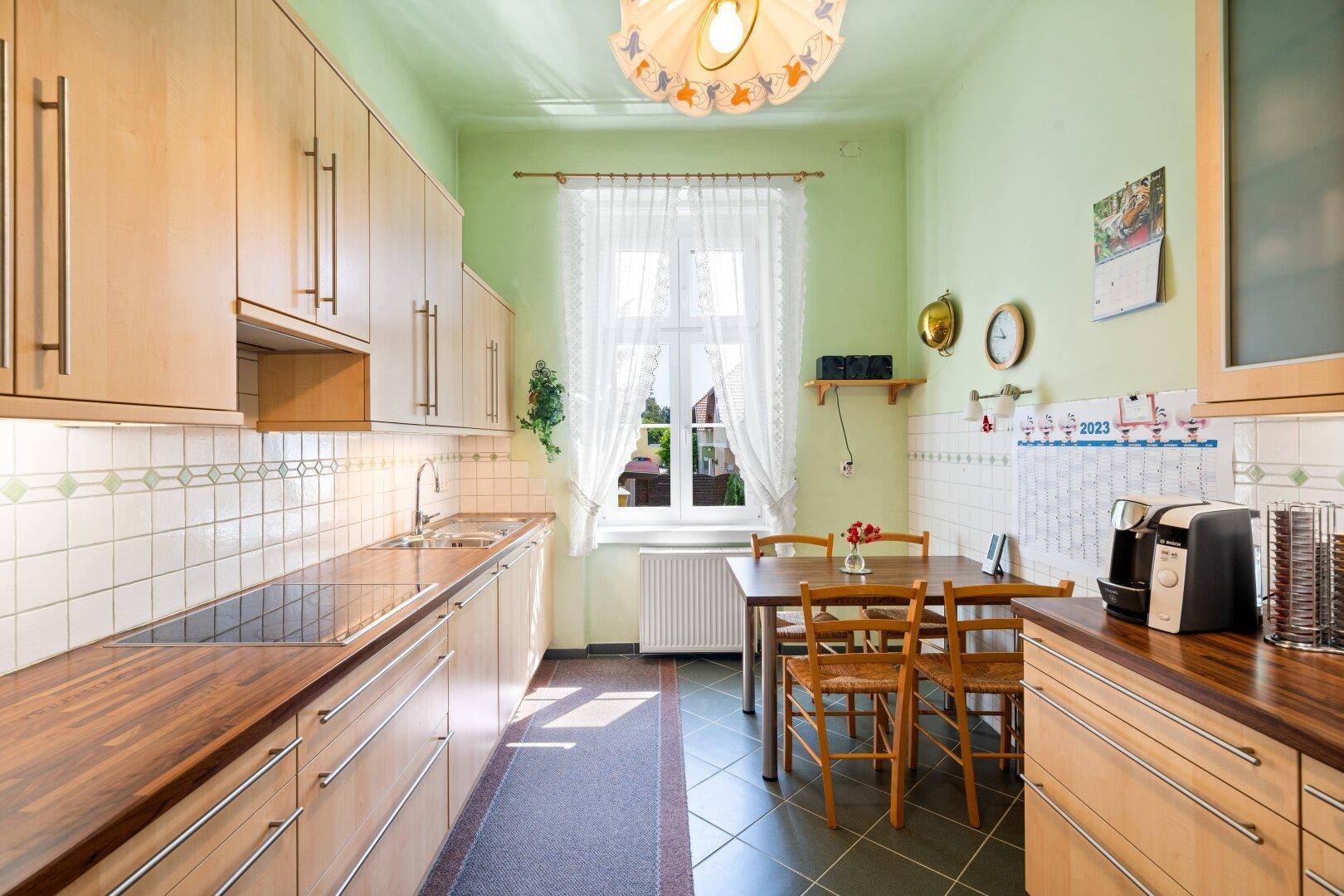 Funktionale Küche mit Holzarbeitsplatten, Fliesenboden und Essbereich am Fenster.