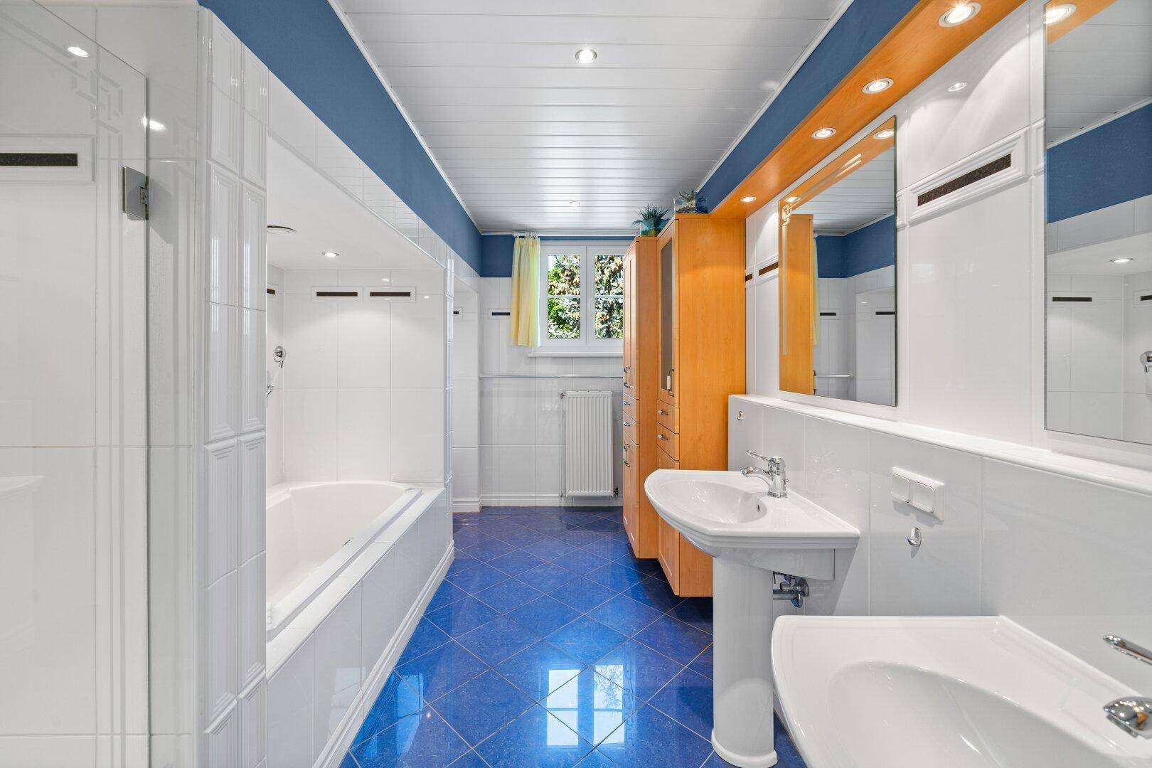 Geräumiges Badezimmer mit blauen Fliesen, Badewanne und zwei Waschbecken.