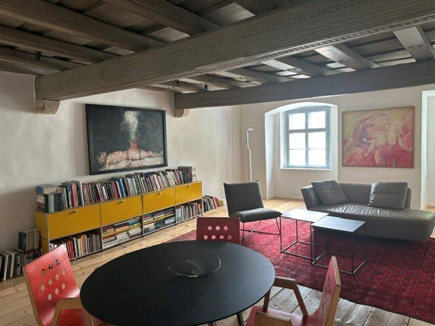 Heller Wohn-Essbereich mit sichtbaren Holzbalken, Holzdielenboden und einem modernen Esstisch.