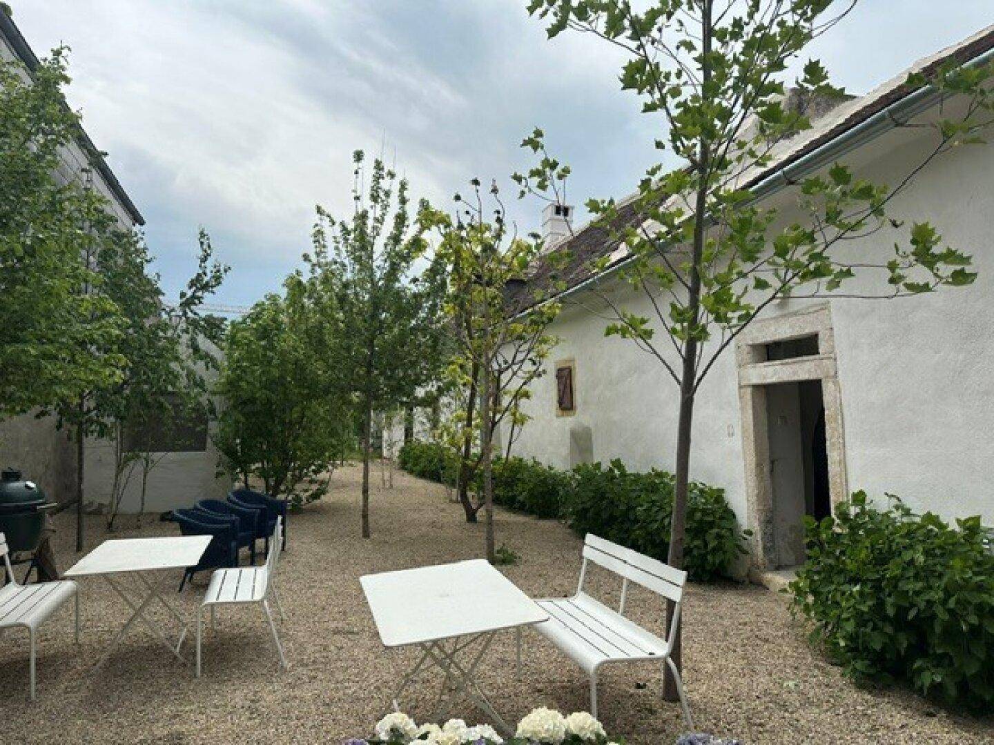 Ruhiger Innenhof mit Kiesboden, jungen Bäumen und weißer Gartenbestuhlung, ideal zum Entspannen.