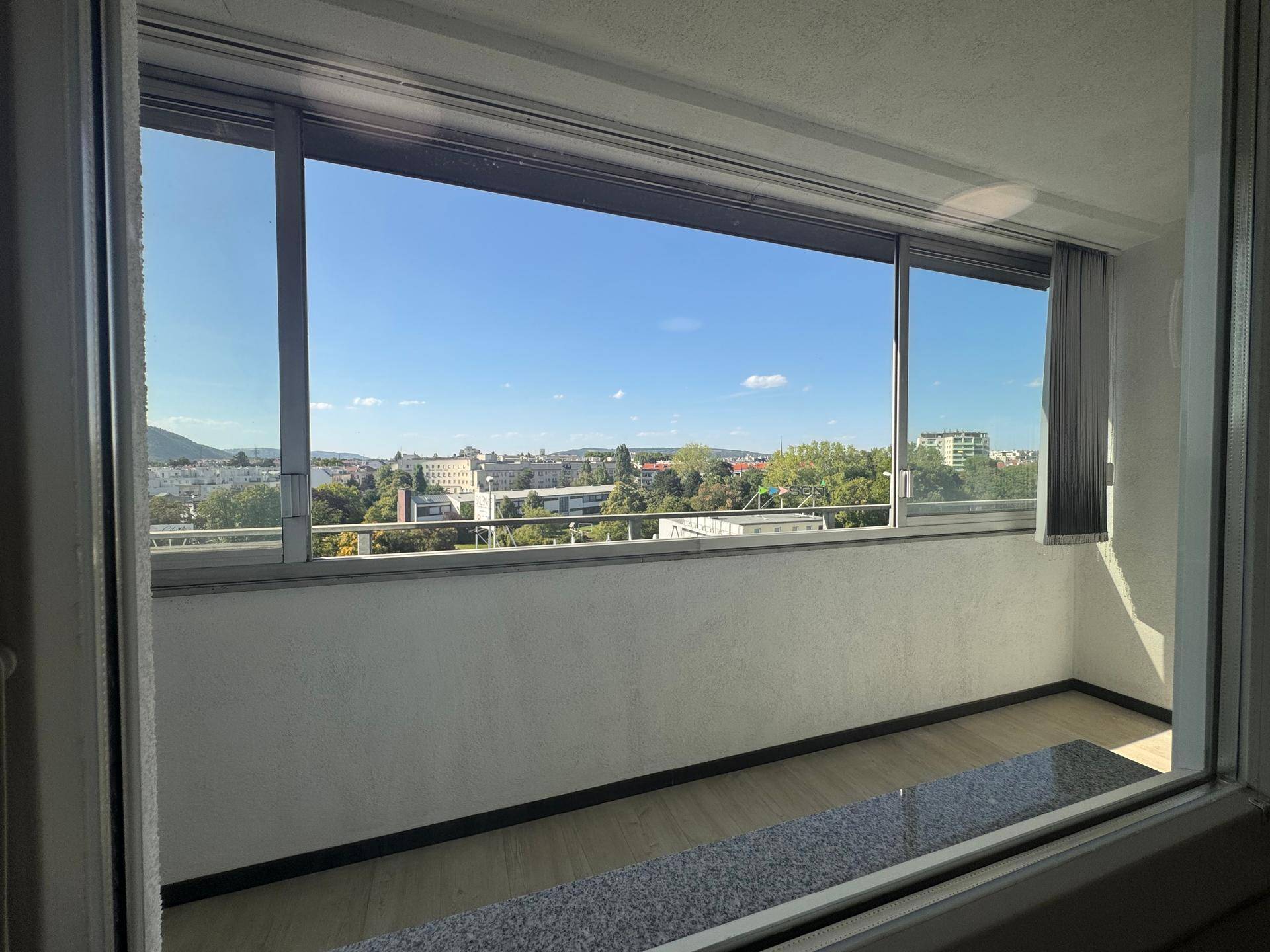 Heller Raum mit weitem Panoramablick über die Stadt und die grüne Umgebung, mit Fensterbank.