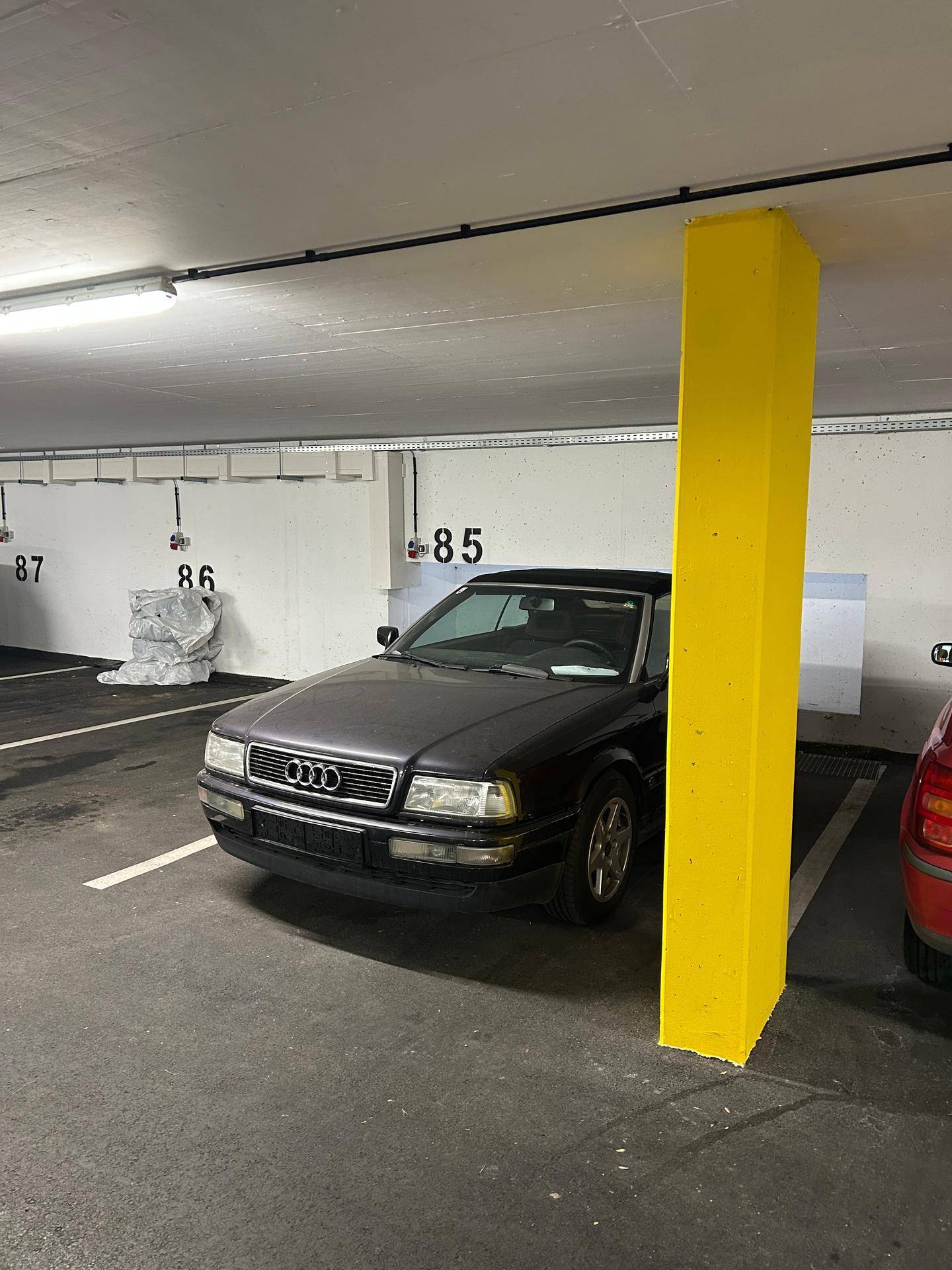 Blick auf einen Tiefgaragenstellplatz mit einem dunklen Auto und einem auffälligen gelben Pfeiler.