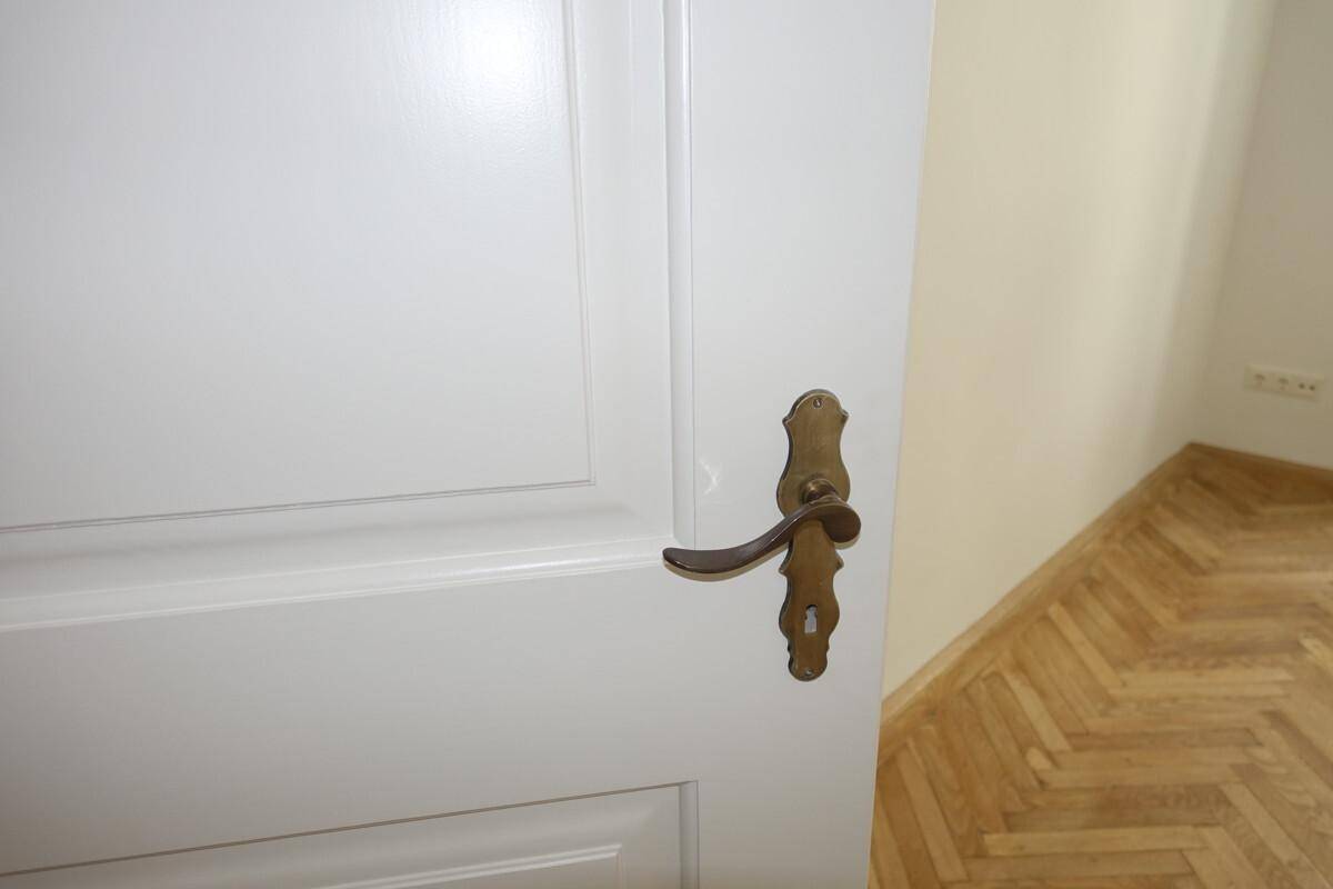 Detailaufnahme einer weißen Tür mit klassischem Messinggriff und Holzboden im Hintergrund.