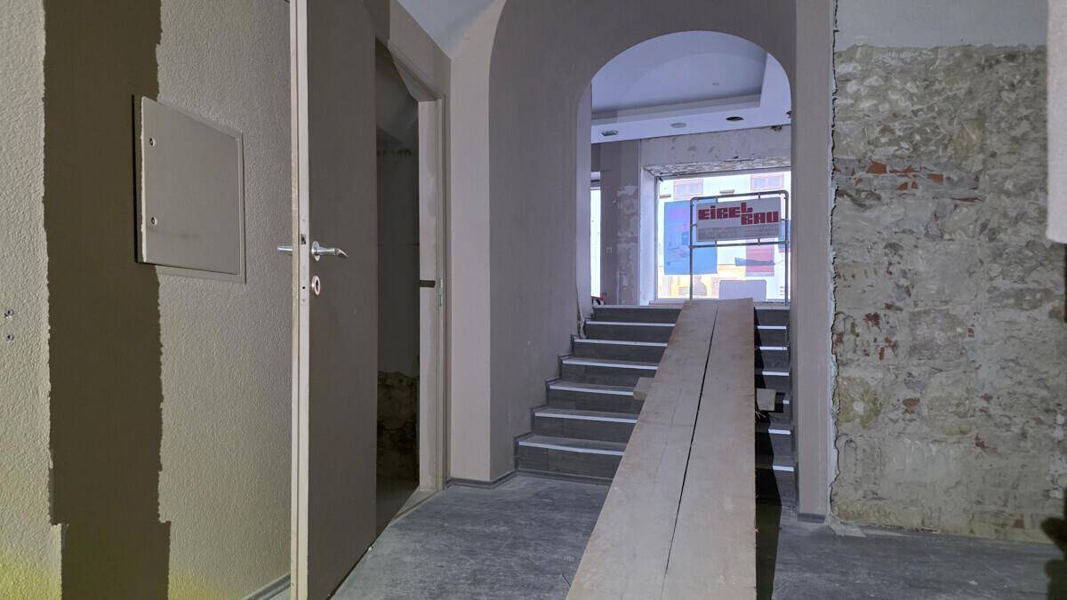 Eingangsbereich mit Treppe und Rampe, der zu einem Ladenlokal im Rohbau führt, mit Blick auf die Straße.