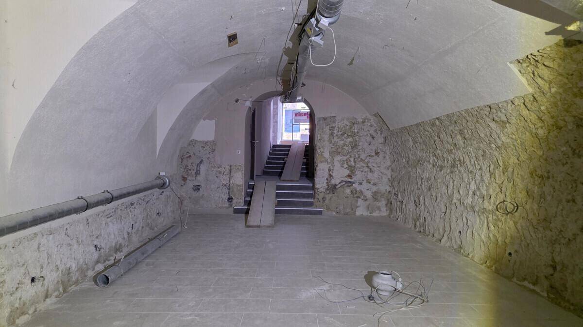 Historischer Kellerraum mit Gewölbedecke, unverputzten Steinwänden und sichtbaren Rohren, im Rohbauzustand.
