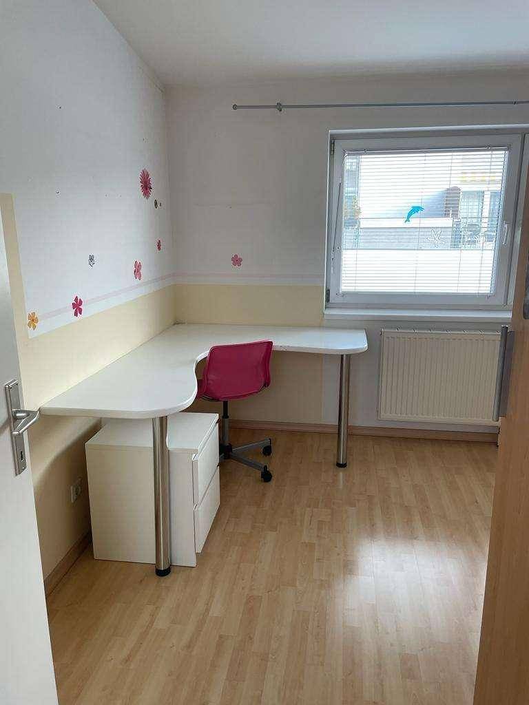 Helles Kinderzimmer oder Büro mit Eckschreibtisch, rotem Stuhl und Fenster.