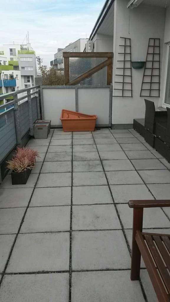 Geräumige Terrasse mit Fliesenboden, Pflanzen und Blick auf die umliegenden Gebäude.