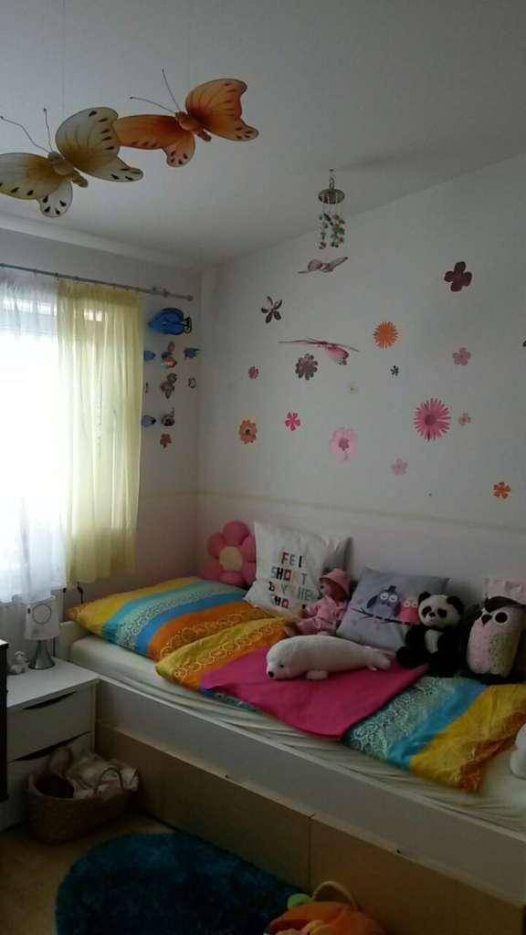 Farbenfrohes Kinderzimmer mit Bett, Spielzeug und Schmetterlingsdekoration an der Decke.
