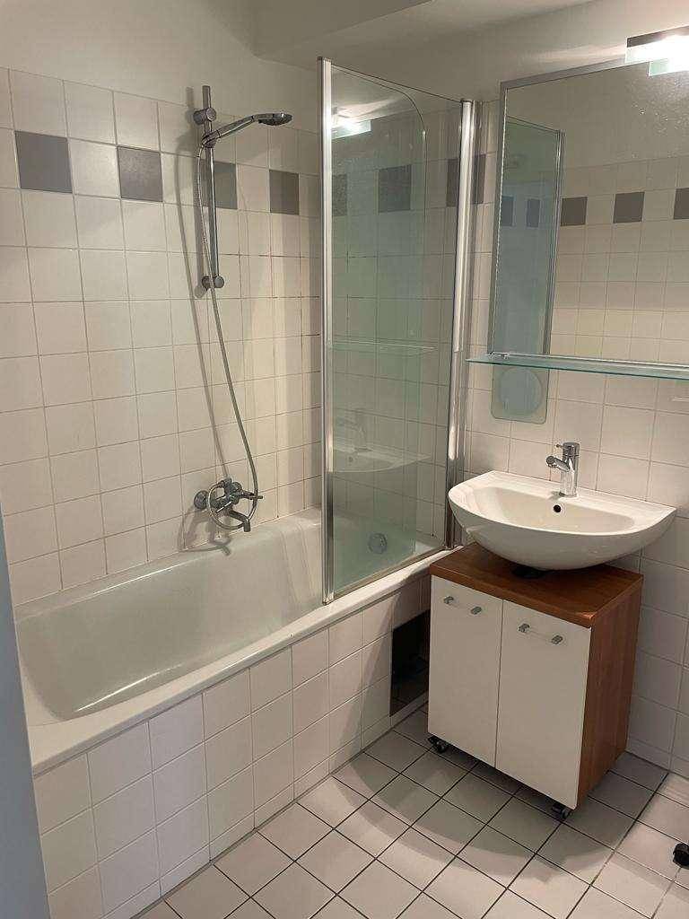 Modernes Badezimmer mit Badewanne, Duschwand und Waschbecken auf Fliesenboden.