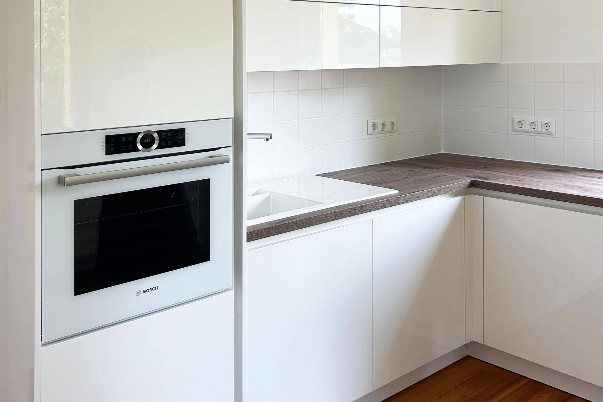 Moderne weiße Küche mit integriertem Backofen von Bosch und dunkler Arbeitsplatte.