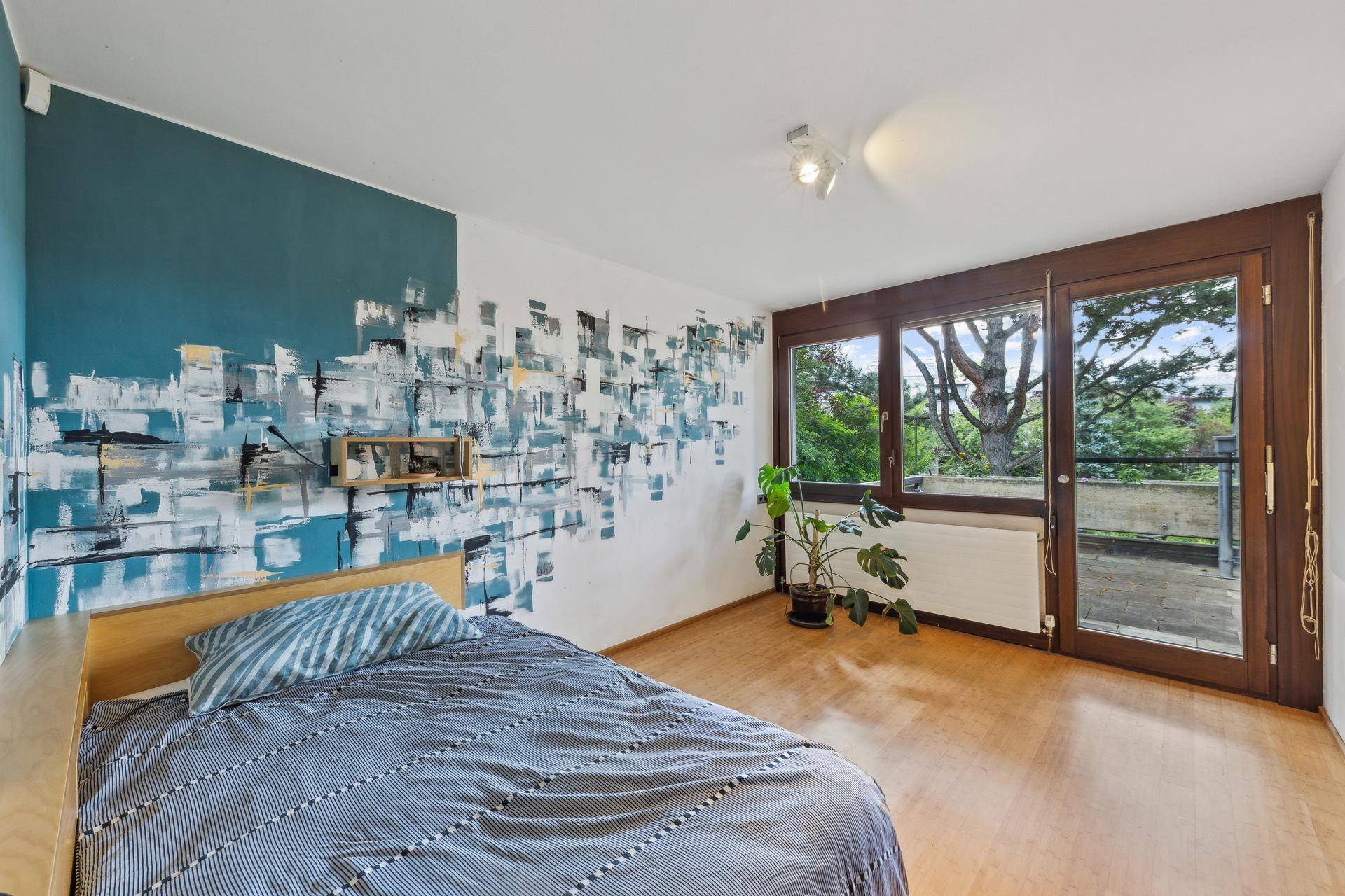 Schlafzimmer mit kreativer Wandgestaltung, Holzboden und direktem Zugang zu einem Balkon.